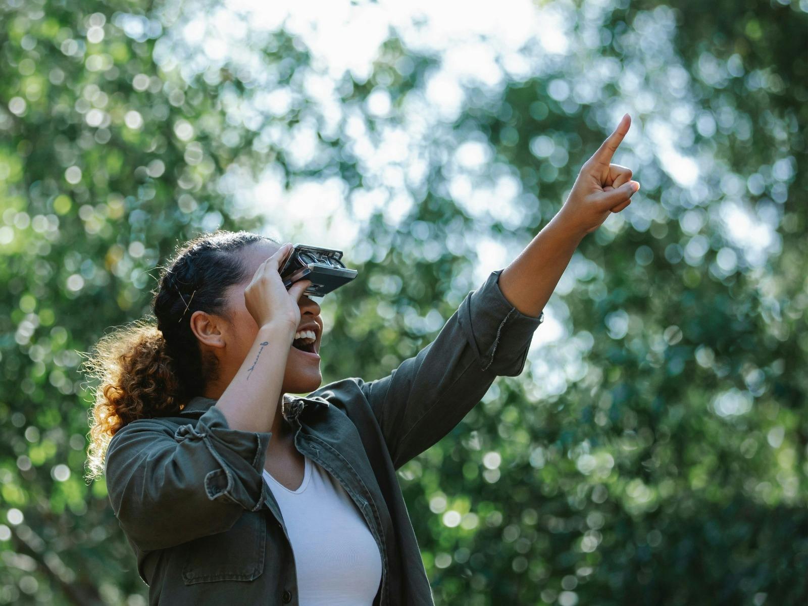 A woman using binoculars is pointing into trees