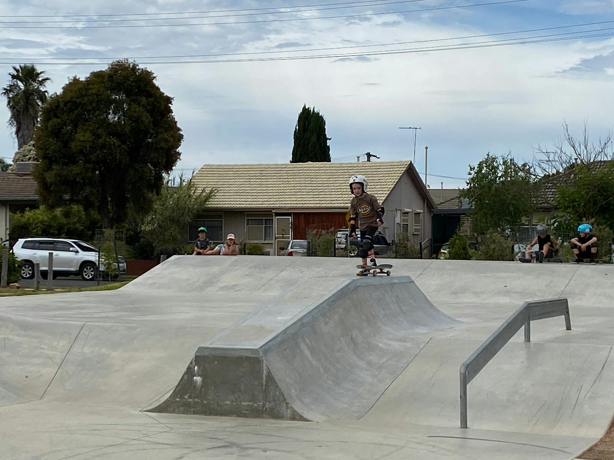 Child using Skateboard on Cement Skate park with other children watching on