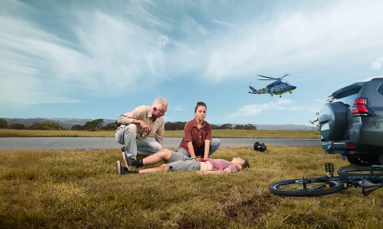 Man and woman helping child in accident on side of road with helicopter in background