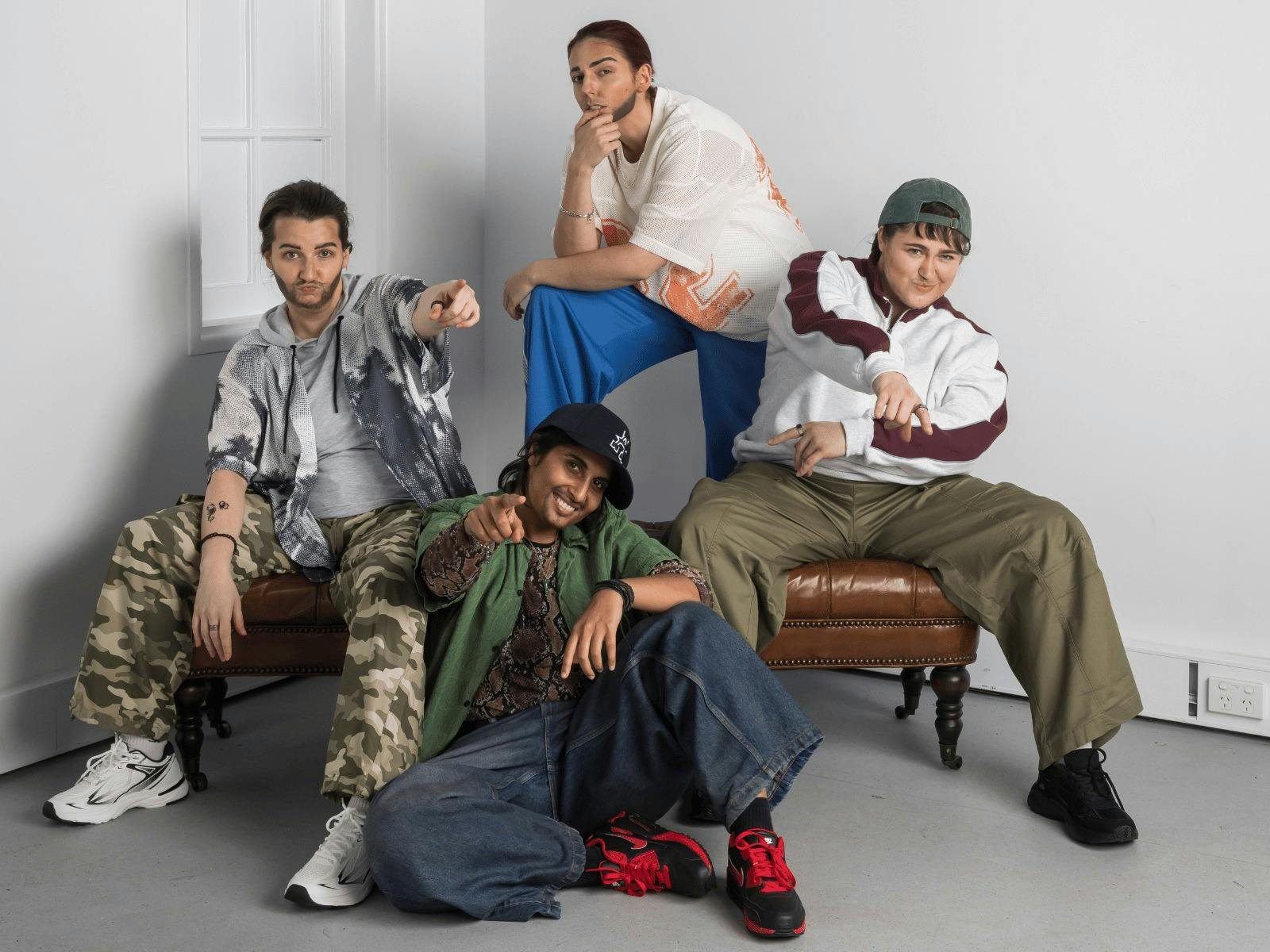Four Drag Kings dressed as boy band members posing on and around a brown leather chair