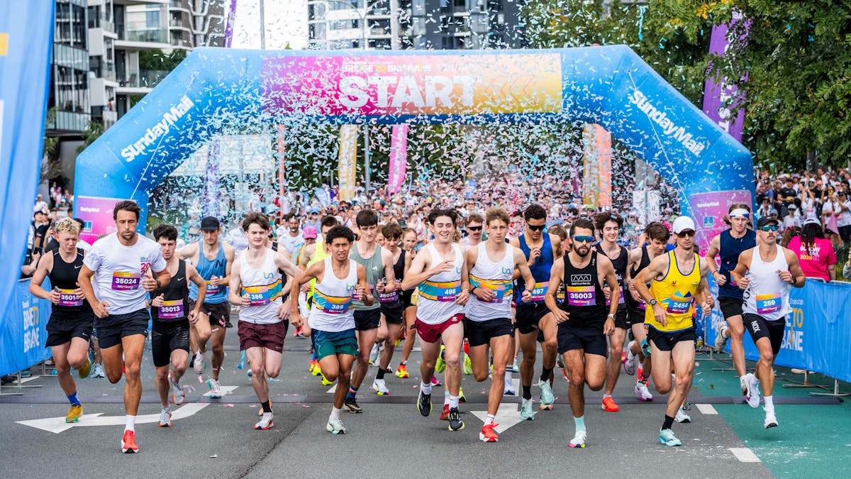 Crowd of runners beginning their race through a start arch. The air is full of confetti.