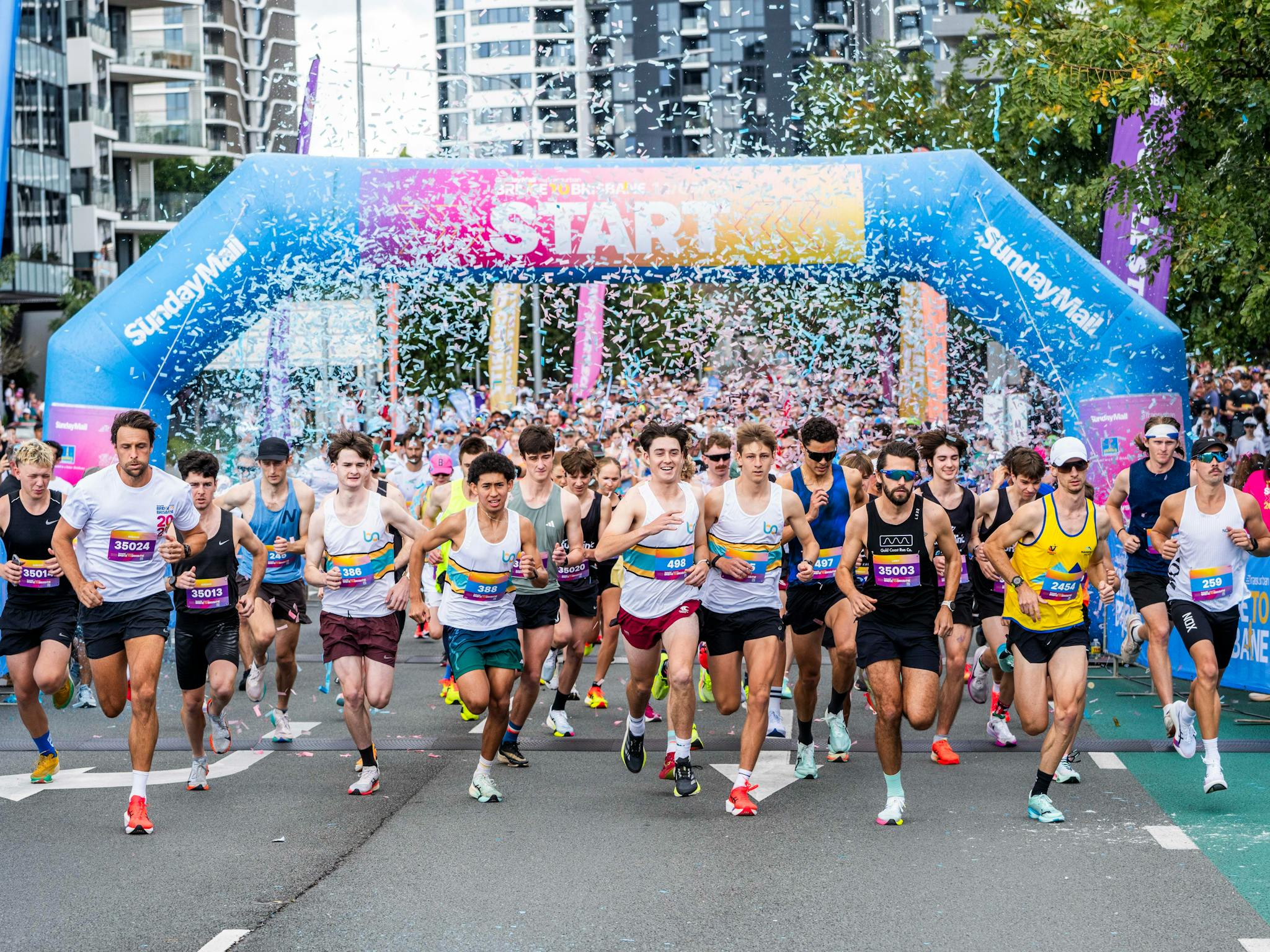 Crowd of runners beginning their race through a start arch. The air is full of confetti. Crowd of runners beginning their race through a start arch. The air is full of confetti.