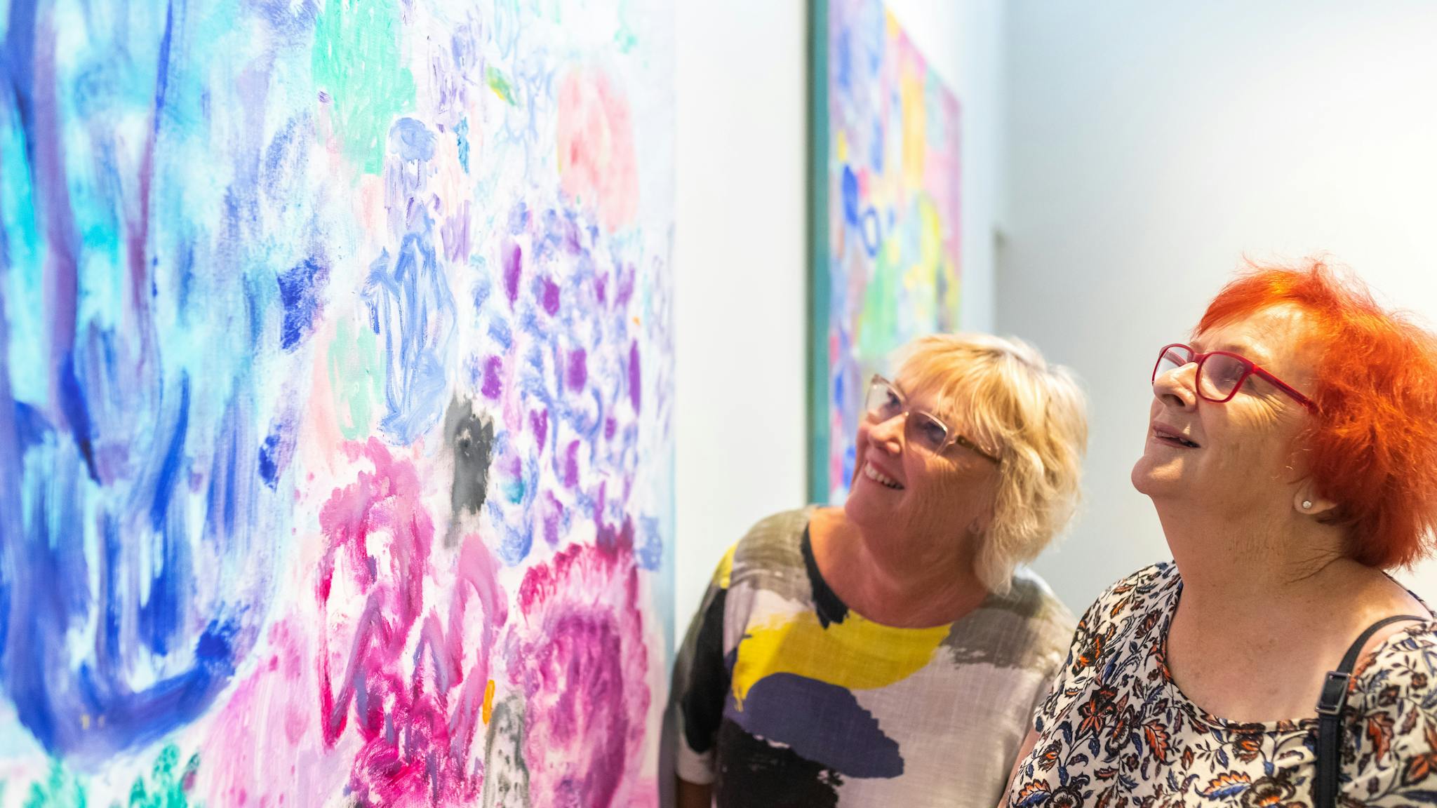 Two women looking closely at colourful artwork