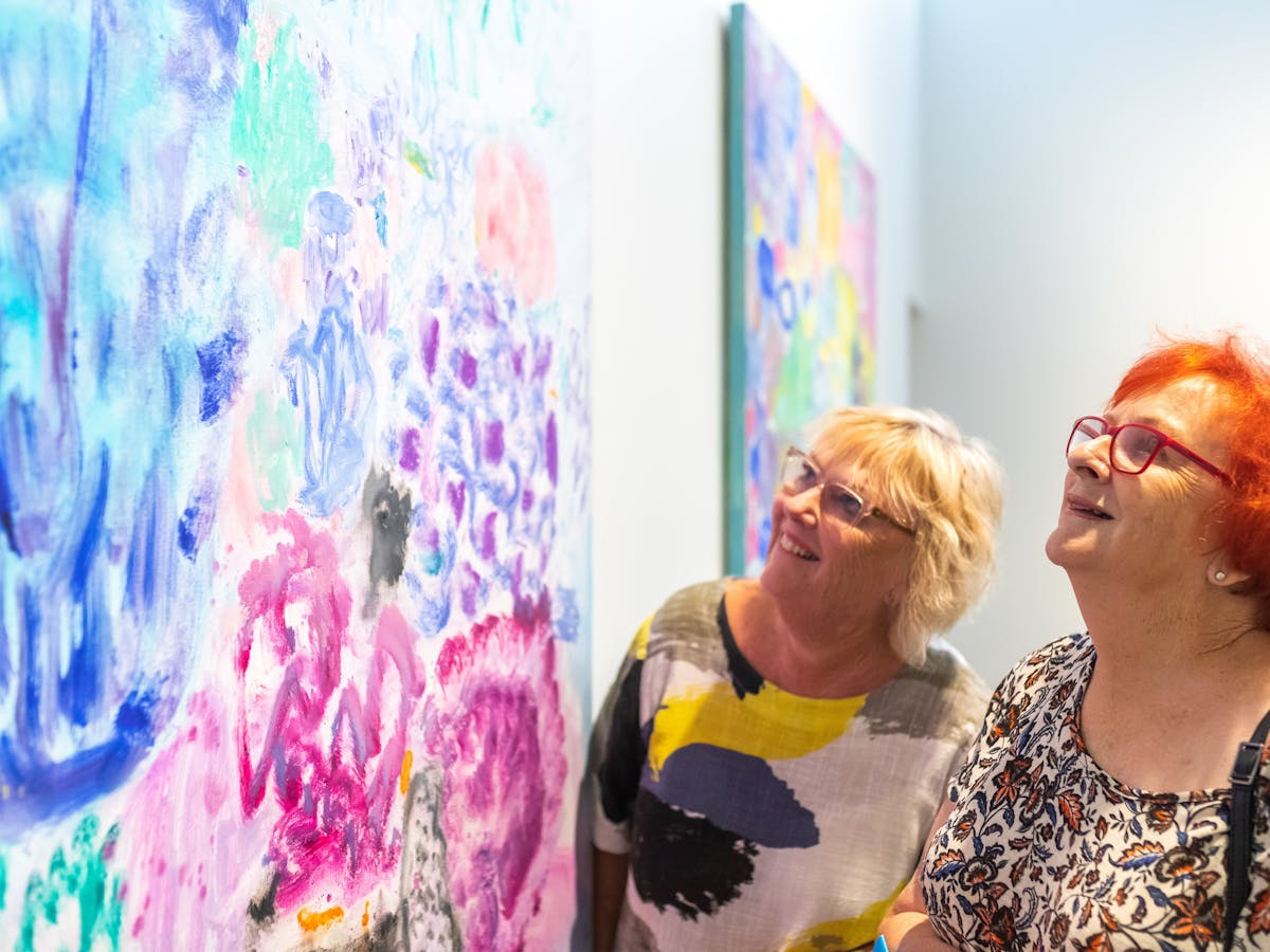 Two women looking closely at colourful artwork
