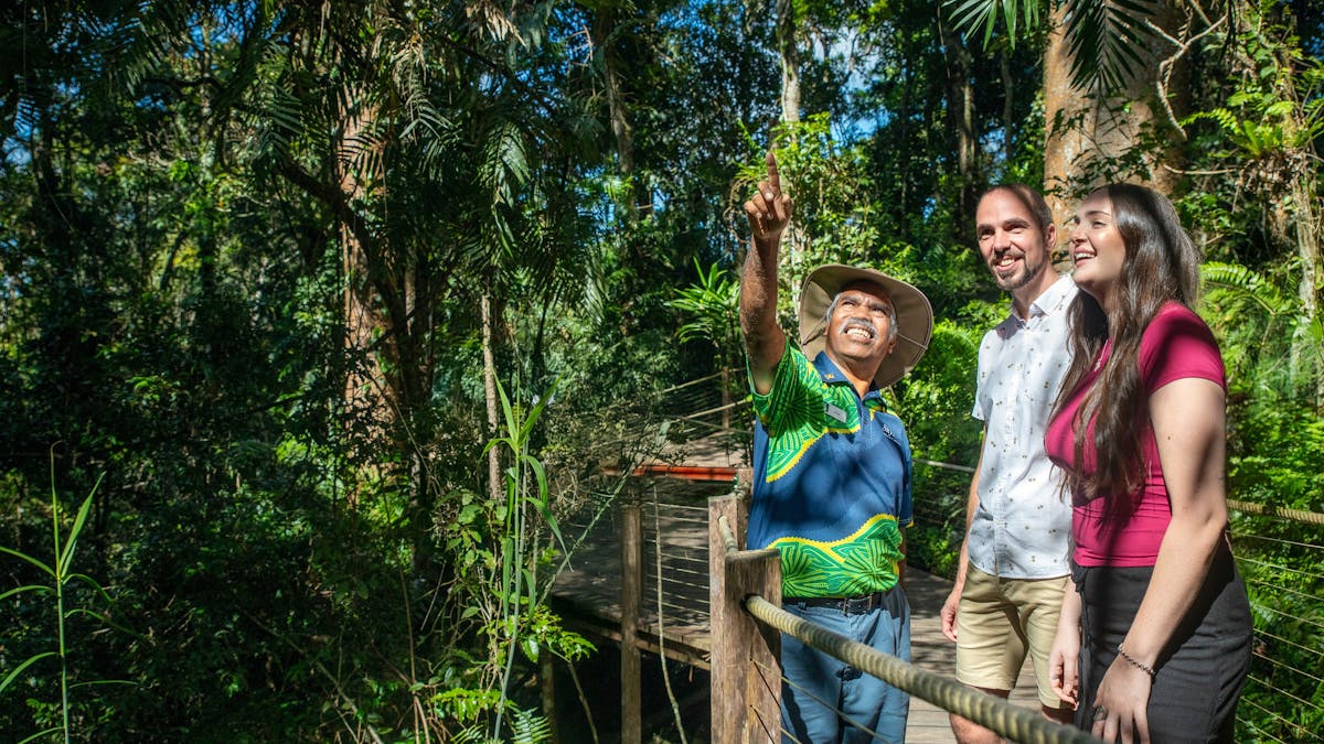 Lady and man standing in the rainforest next to a Ranger Guide pointing up