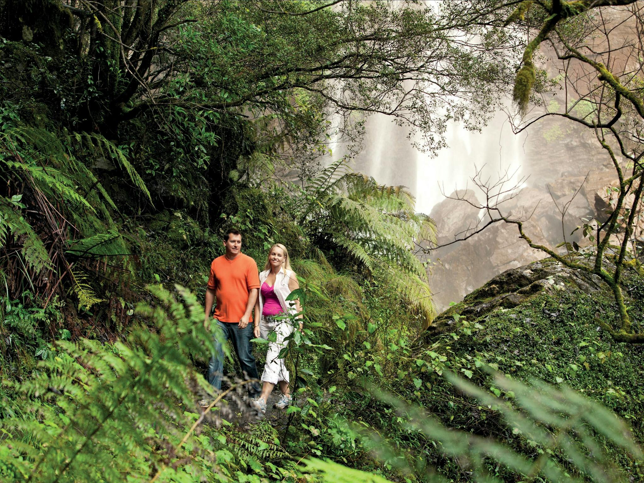Couple walking through forest at base of falls.