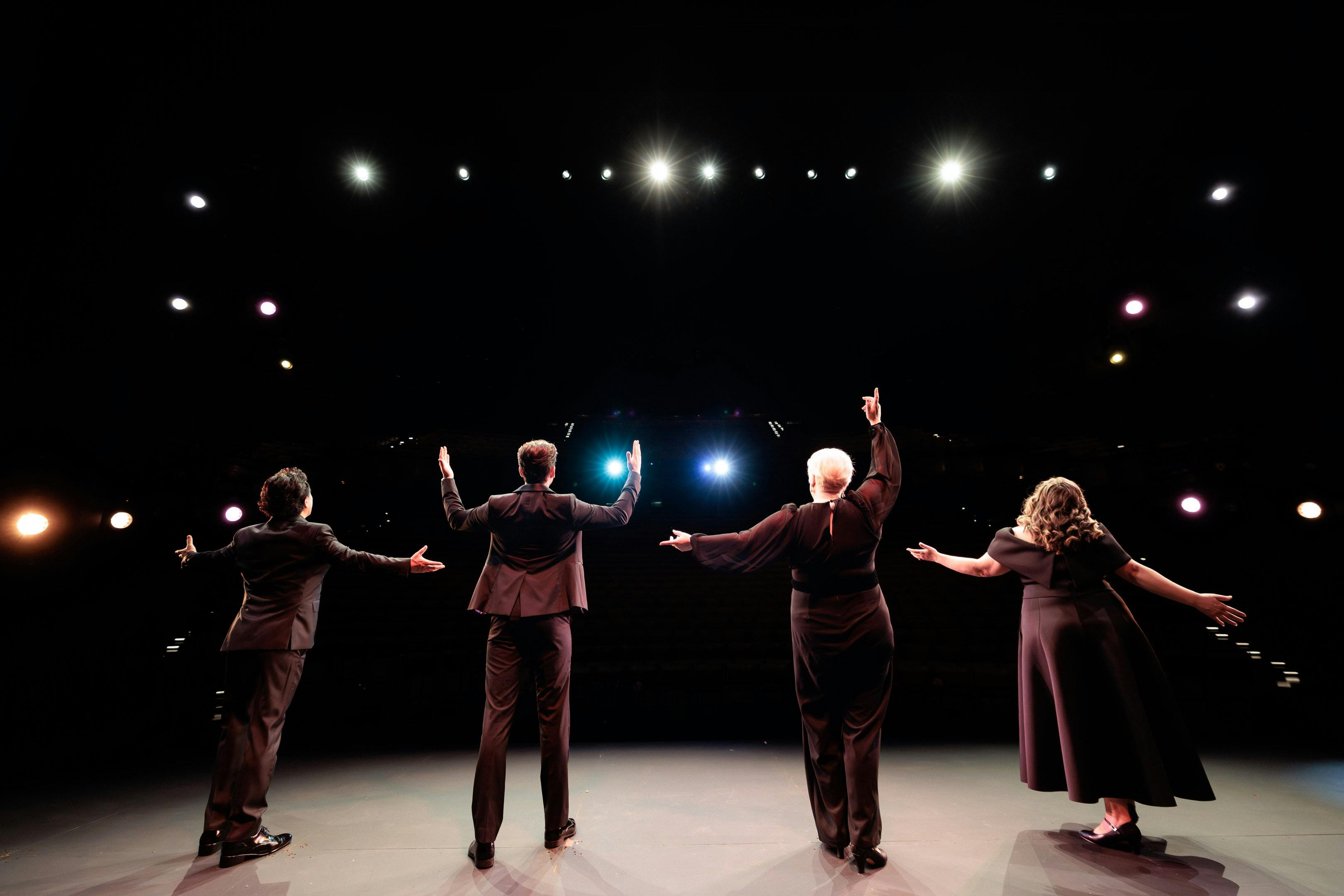 We see 4 Opera singers in black from behind taking their curtain call in front of the audience