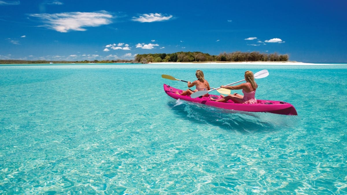 Two ladies Kayak in a pink kayak on the crystal clear turquoise waters of Wathumaba Creek, K'gari
