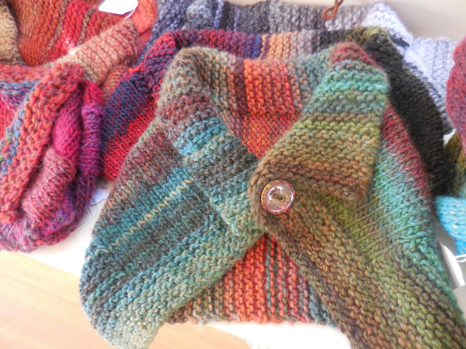 A rainbow coloured, hand-knitted neckwarmer with button