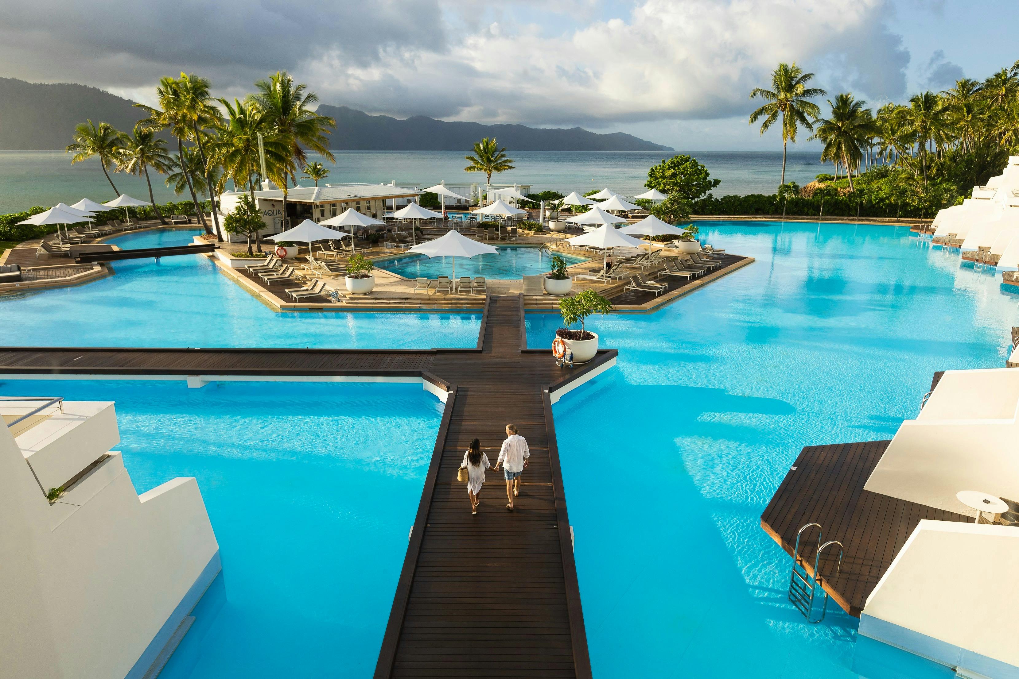 Couple walking along the footpath located in the middle of a large resort pool