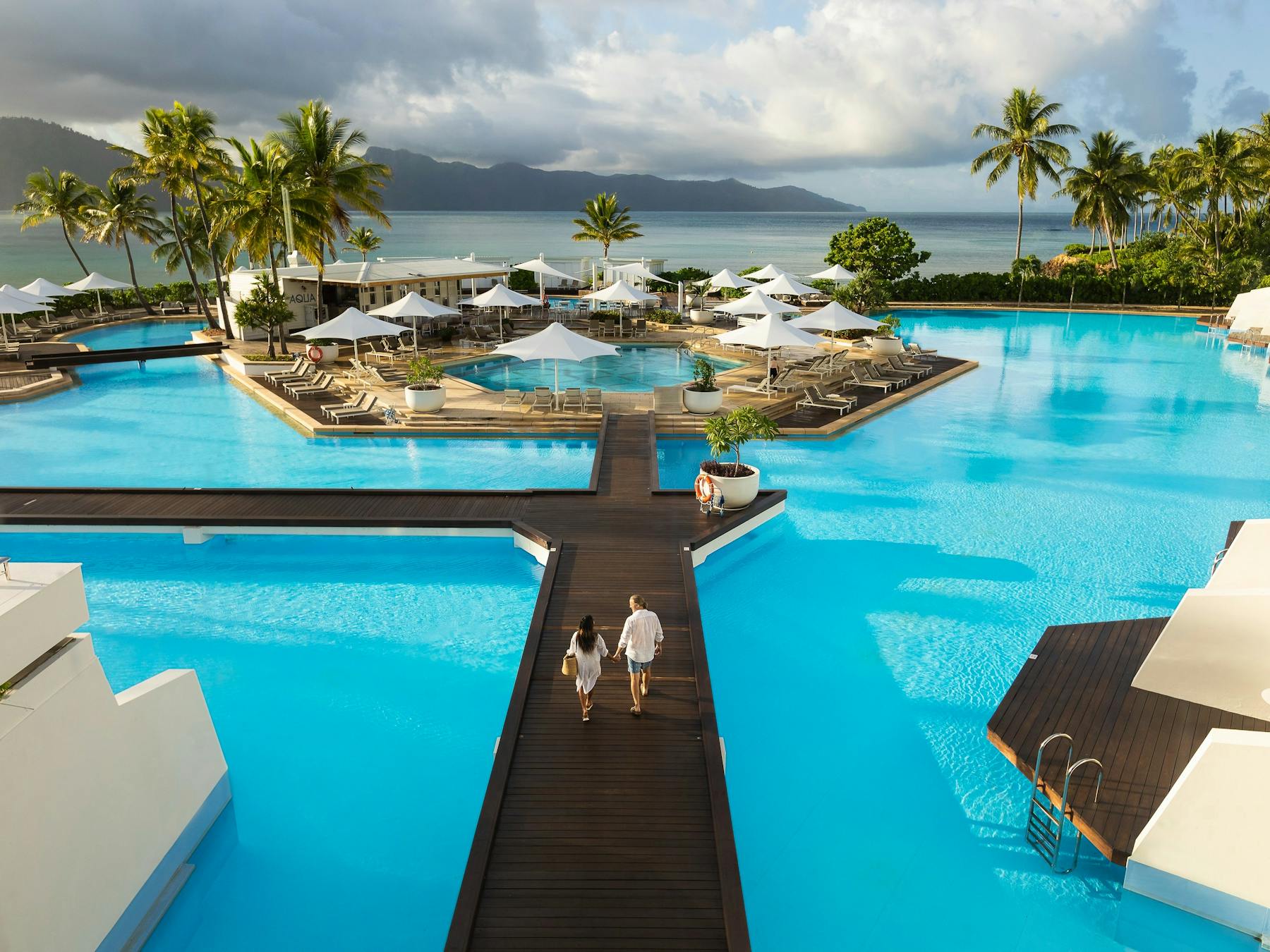 Couple walking along the footpath located in the middle of a large resort pool