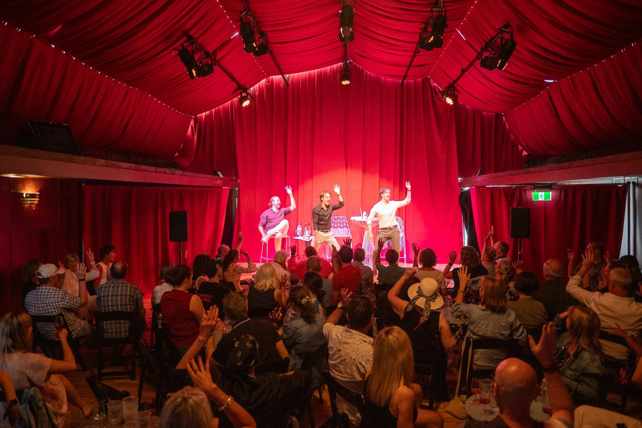 Crowd watching three men on stage with hands raised