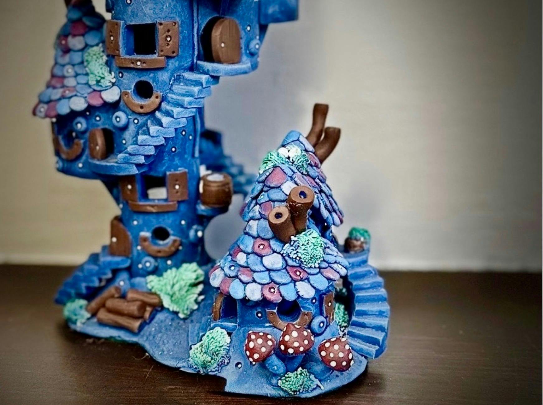A fairy House sculpture in blue and purple with tiny details of tiled roofs, stairways and mushrooms