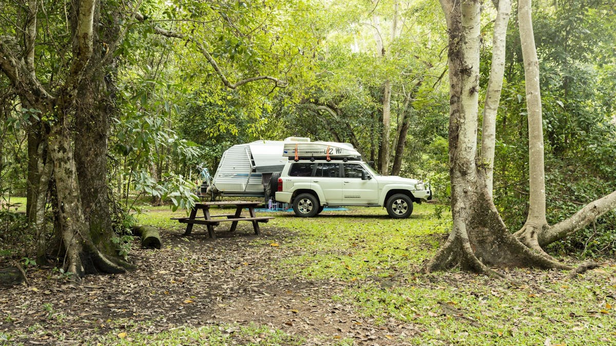 Four-wheel-drive vehicle with boat on top parked in front of a caravan. There's a picnic table too.