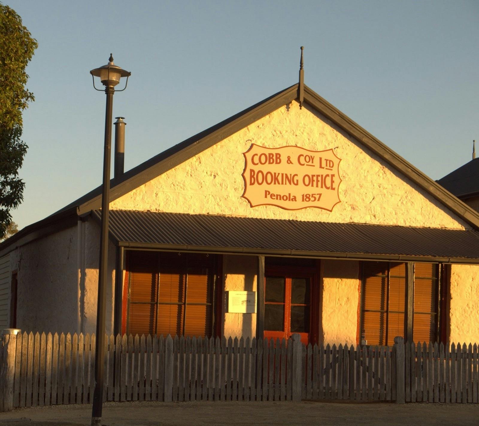 A sunset photo of the old Cobb & Co building. It has a sign on the front Booking office Penola 1857.