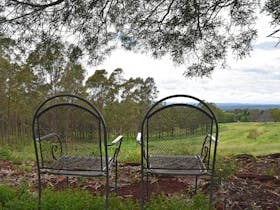 two chairs overlooking a green valley with trees cloudy sky