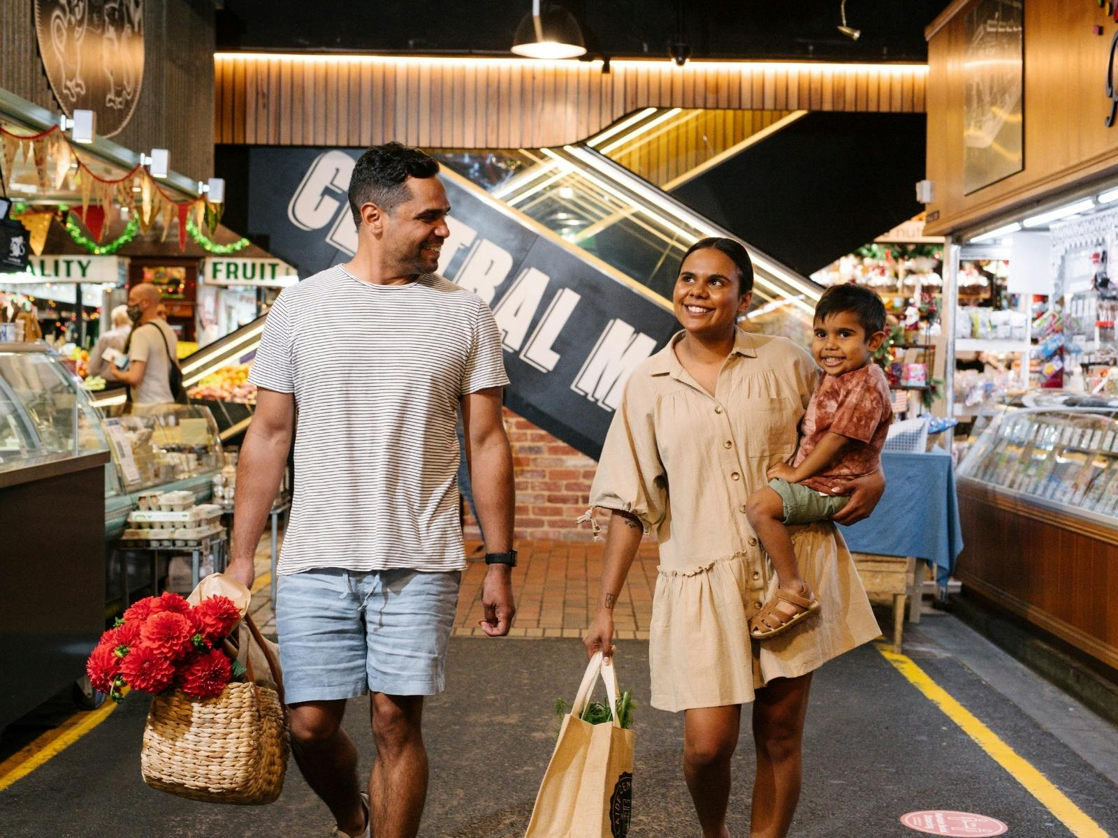 Young couple carrying child and shopping walk through market