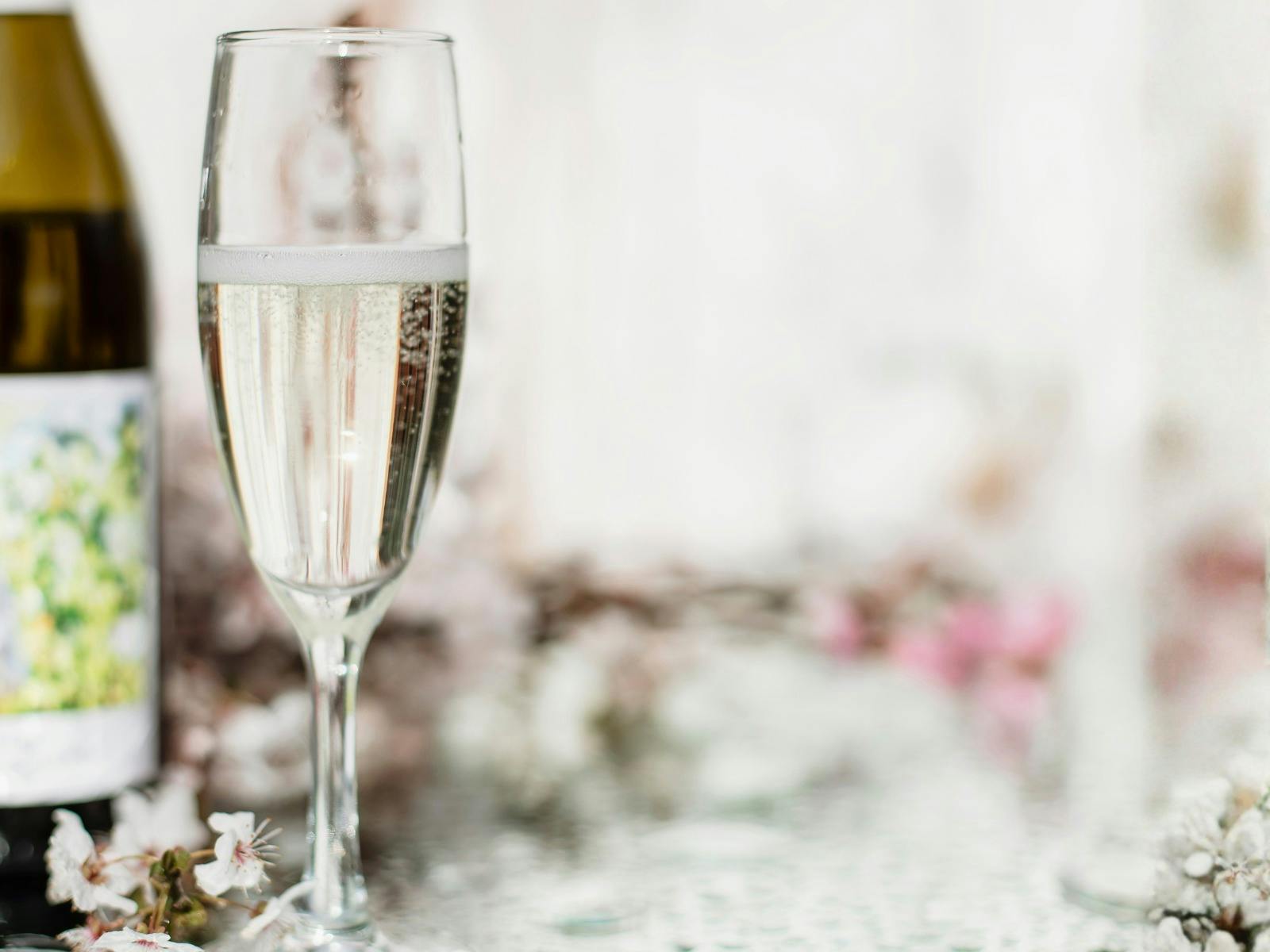 Glass of sparkling wine next to bottle with a mirror as a table and floral arrangements