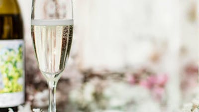 Glass of sparkling wine next to bottle with a mirror as a table and floral arrangements