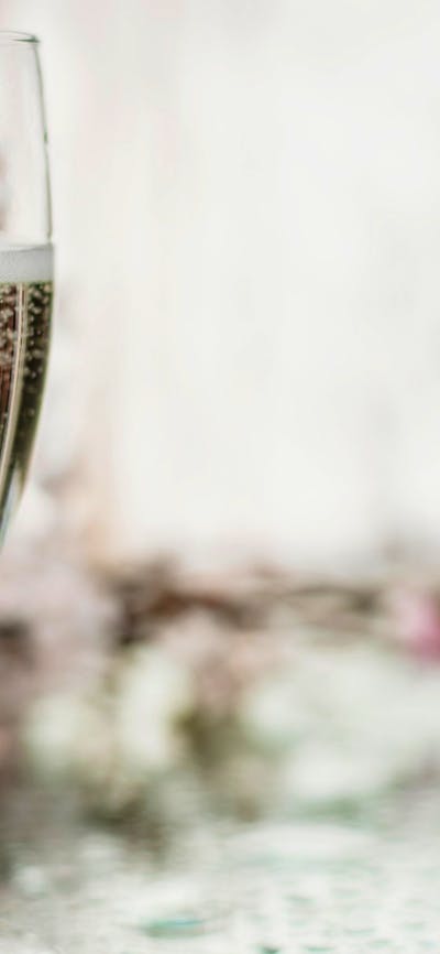 Glass of sparkling wine next to bottle with a mirror as a table and floral arrangements