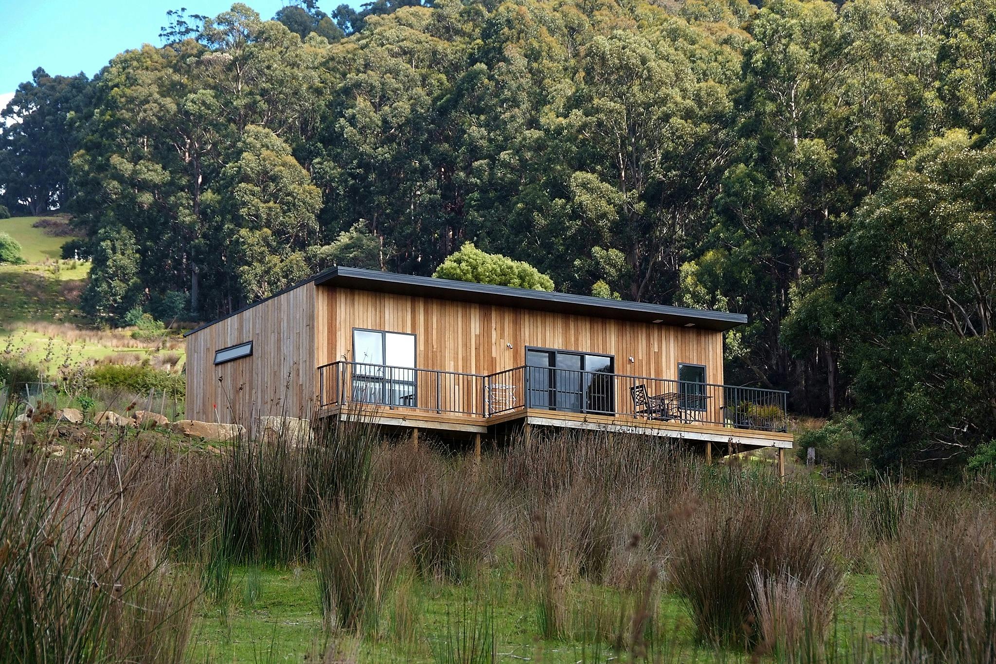 Timber cottage on hillside, showing deck and forest in background