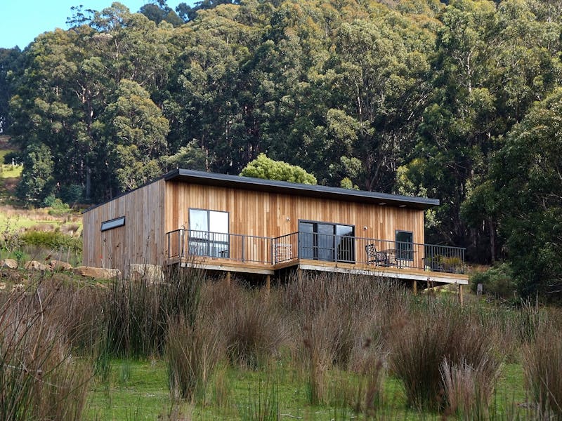 Timber cottage on hillside, showing deck and forest in background