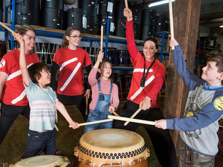 Three kids use bachi sticks to hit taiko drums