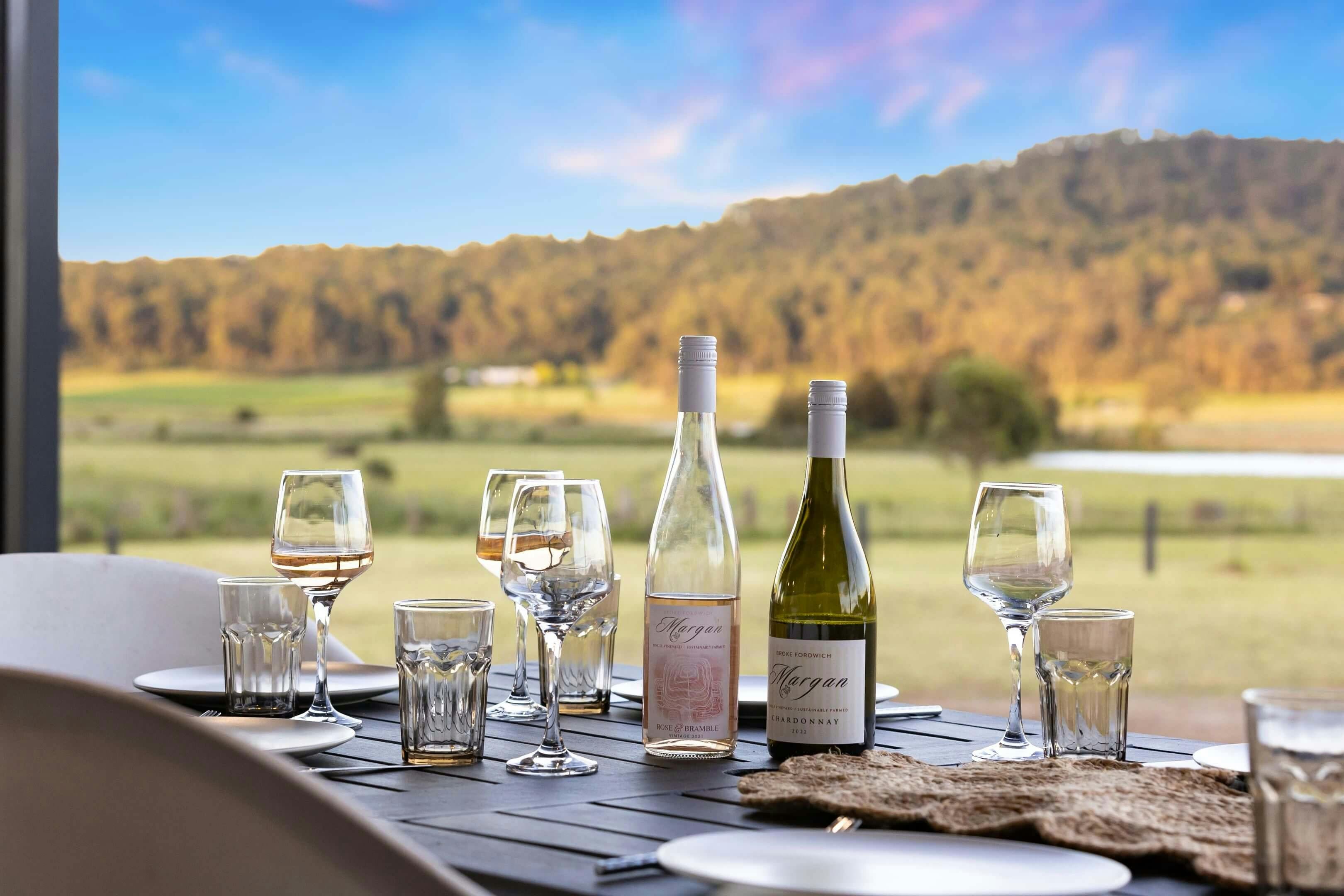 outdoor dining table with wine bottles, glasses, and plates overlooks a scenic landscape