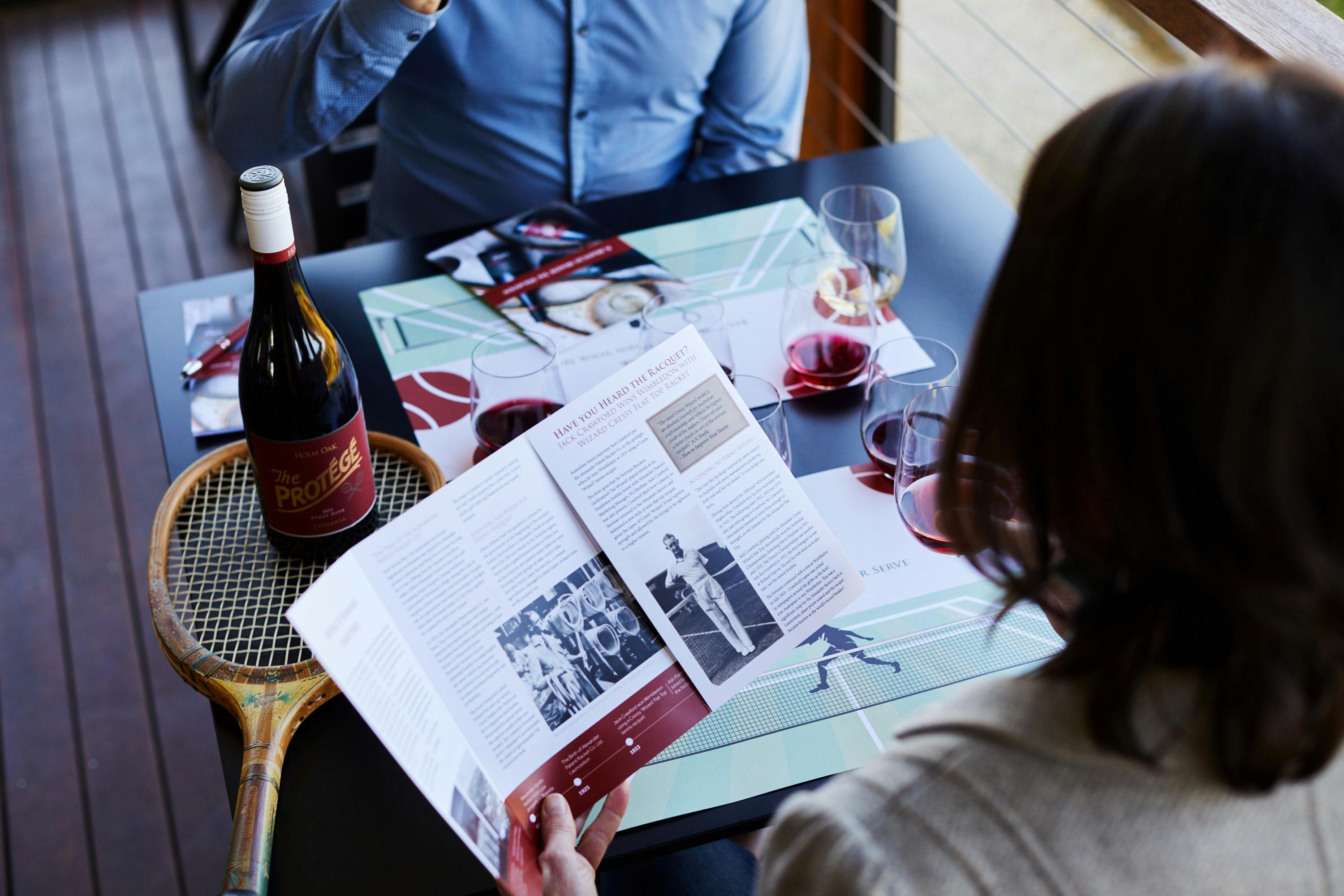 Lady reading brochure contining tennis history with wine glass hin her hand.