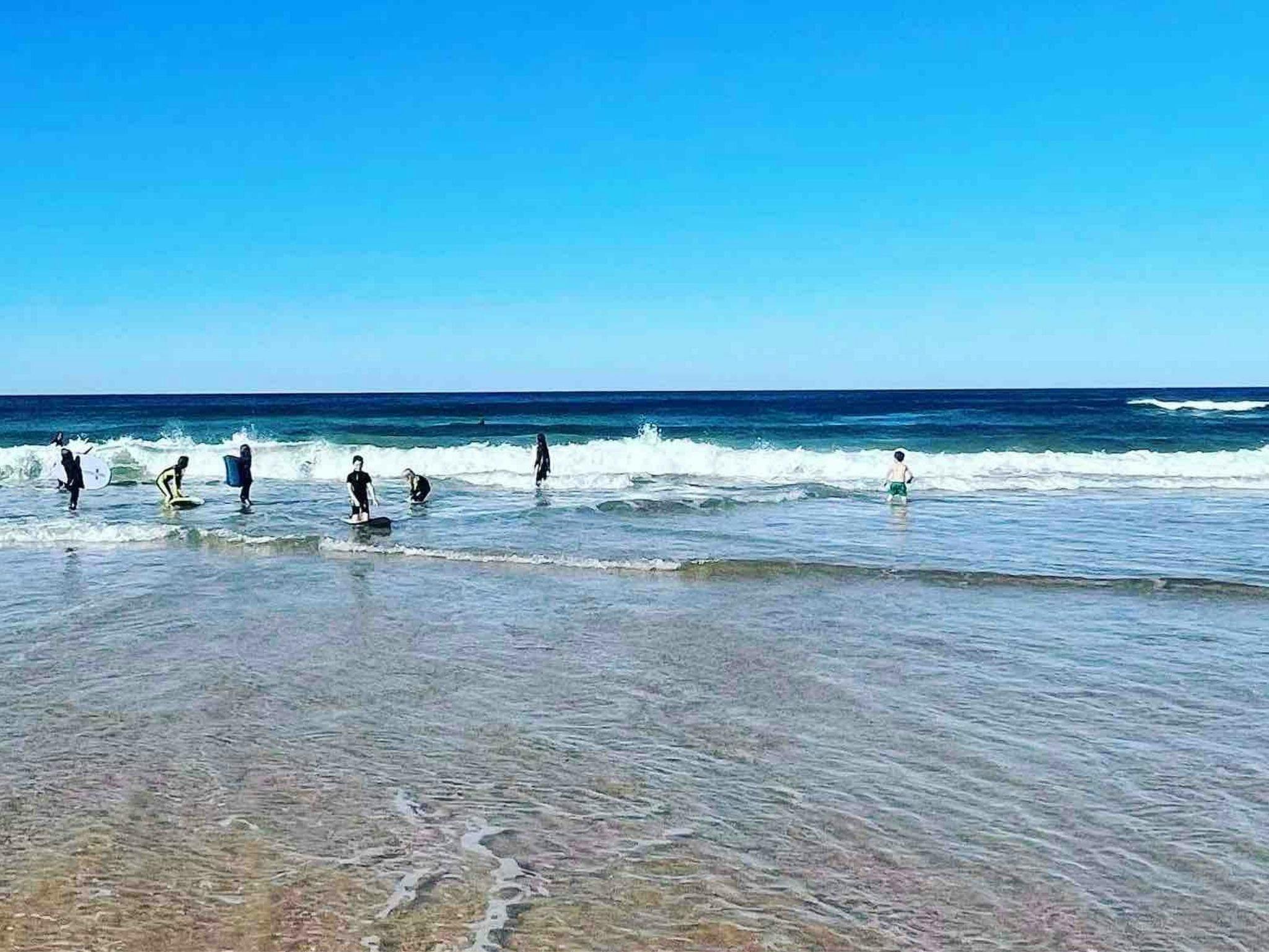 Several kids riding foam surfboards in small swell.