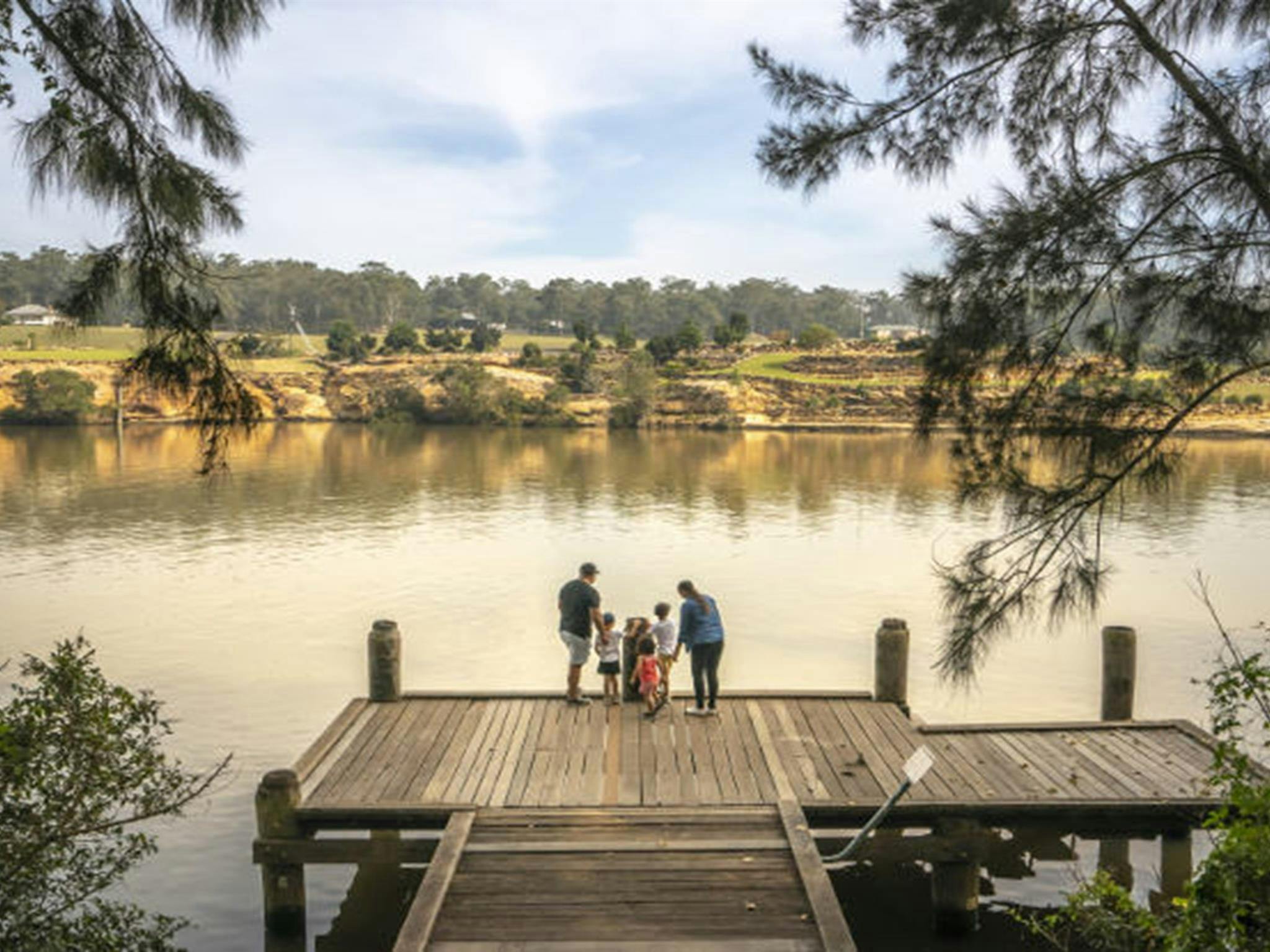 Eine Familie steht auf einem hölzernen Steg und blickt über den Hawkesbury River am Picknickplatz der Cattai Farm
