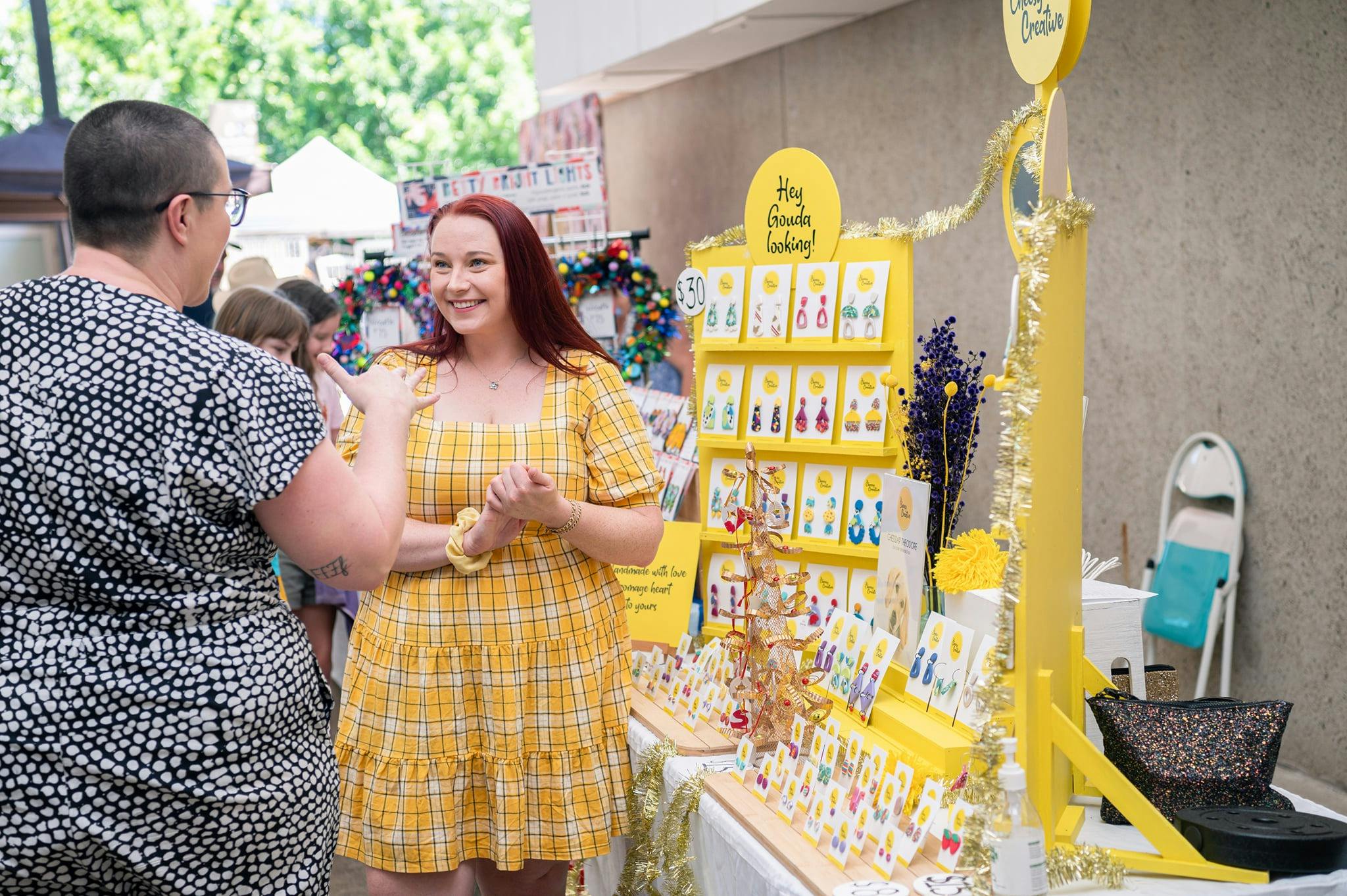Stall holder talks with customer in from of yellow earring stall