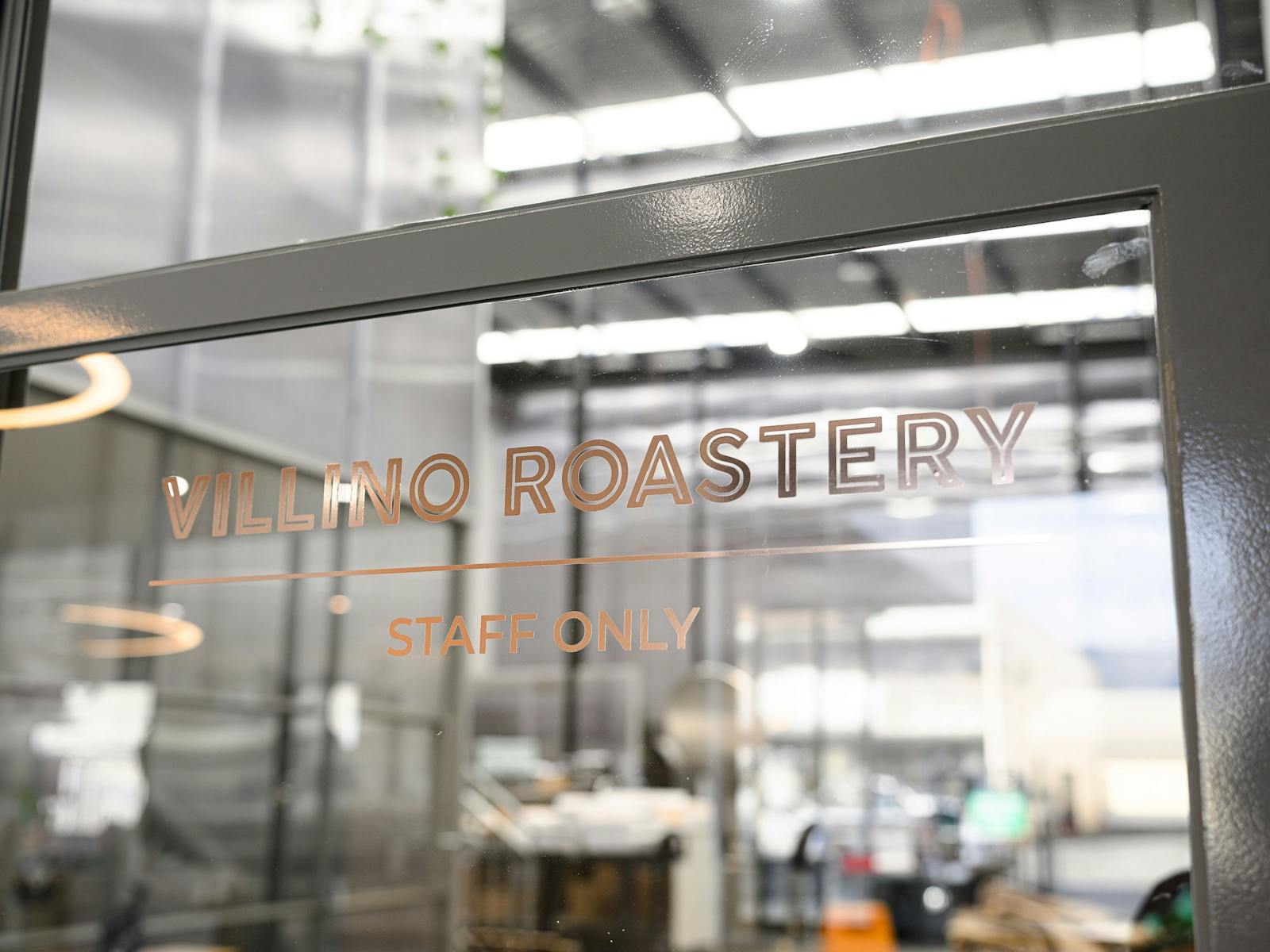 A Staff Only sign on a glass door with rose gold decals reading Villino Roastery.