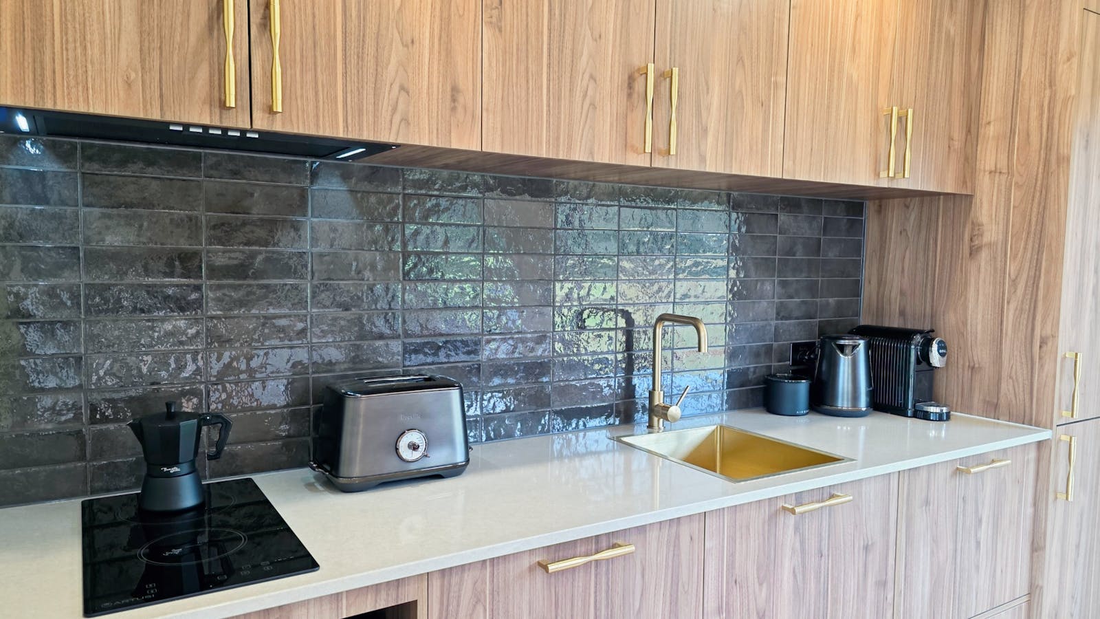 Stone benchtop kitchenette with induction cooktop, dishwasher, fridge and coffee pod machine