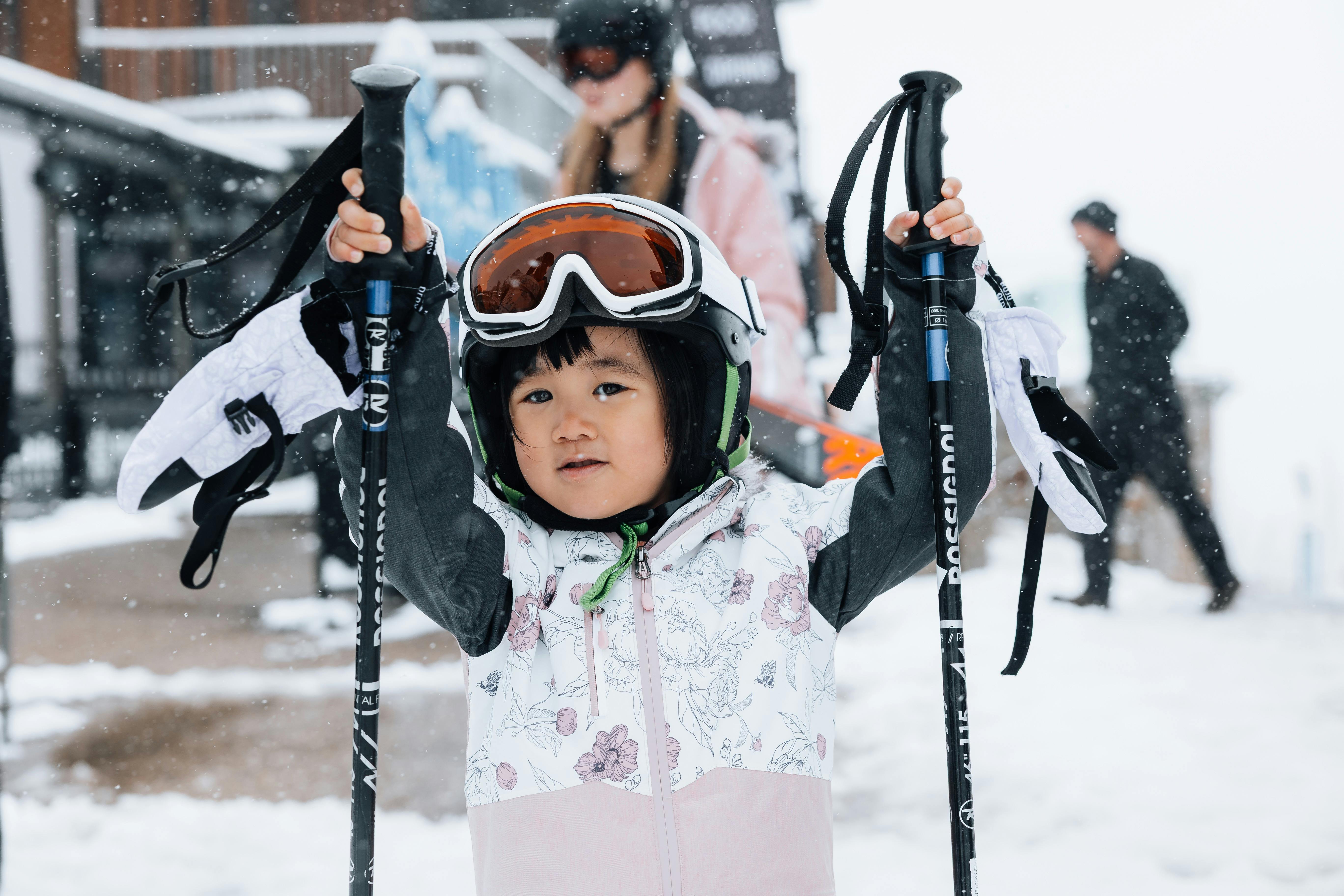 Young child holding ski poles, wearing goggles and helmet ready to go skiing