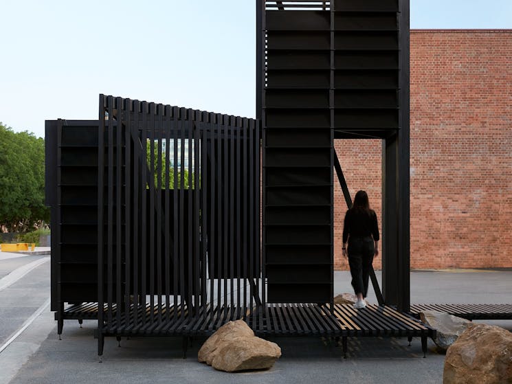 Modular installation situated outdoors with a figure standing in an opening on the right side