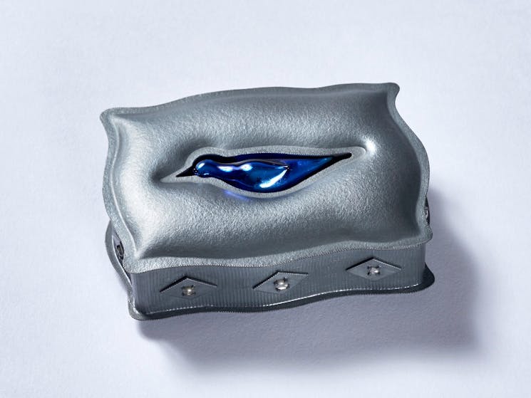 A metal pillow with a blue bird in the middle and diamonds inserts around the edges