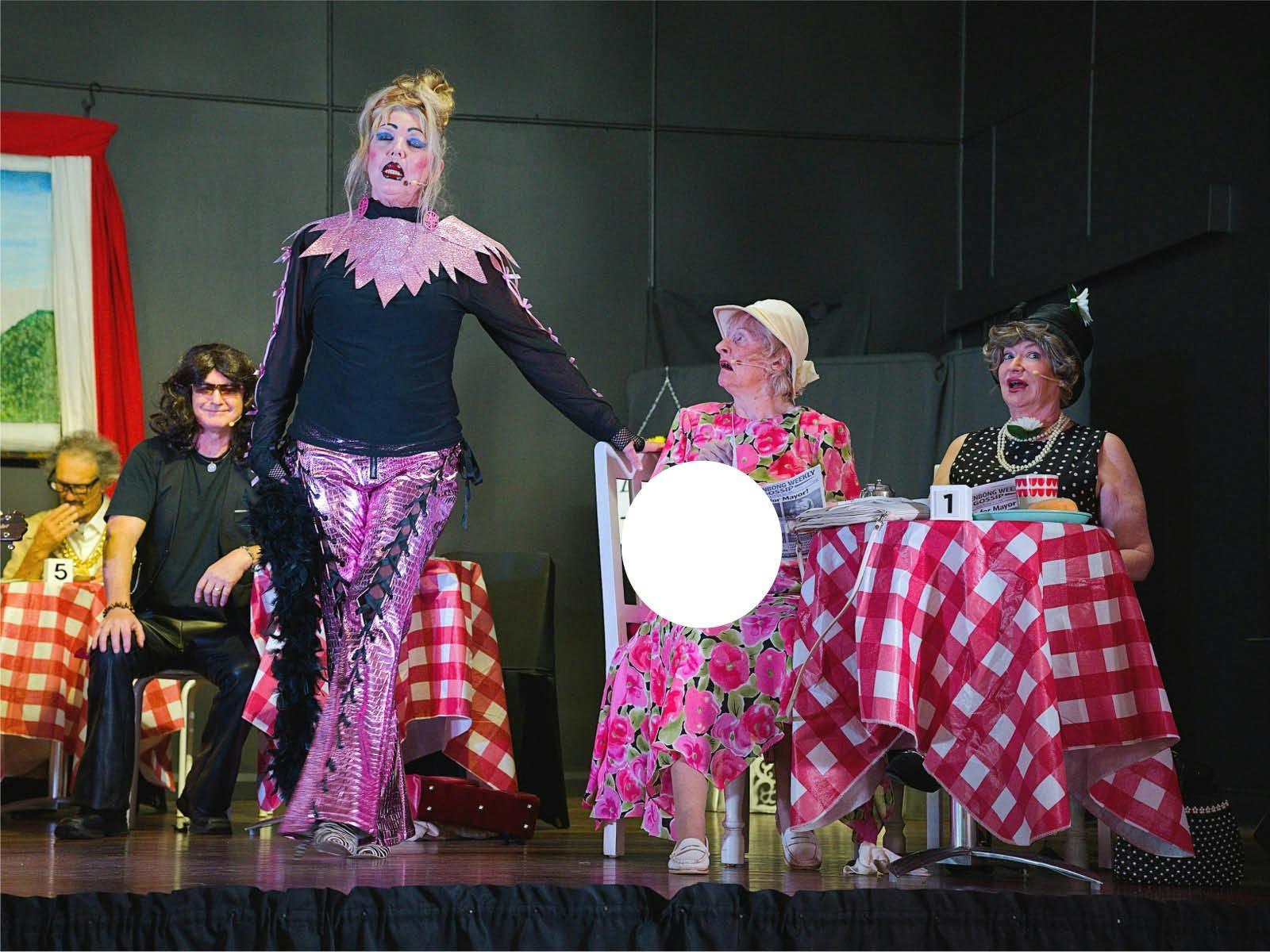 5 actors on a stage in a variety of outfits sitting at cafe tables with red and white check cloths