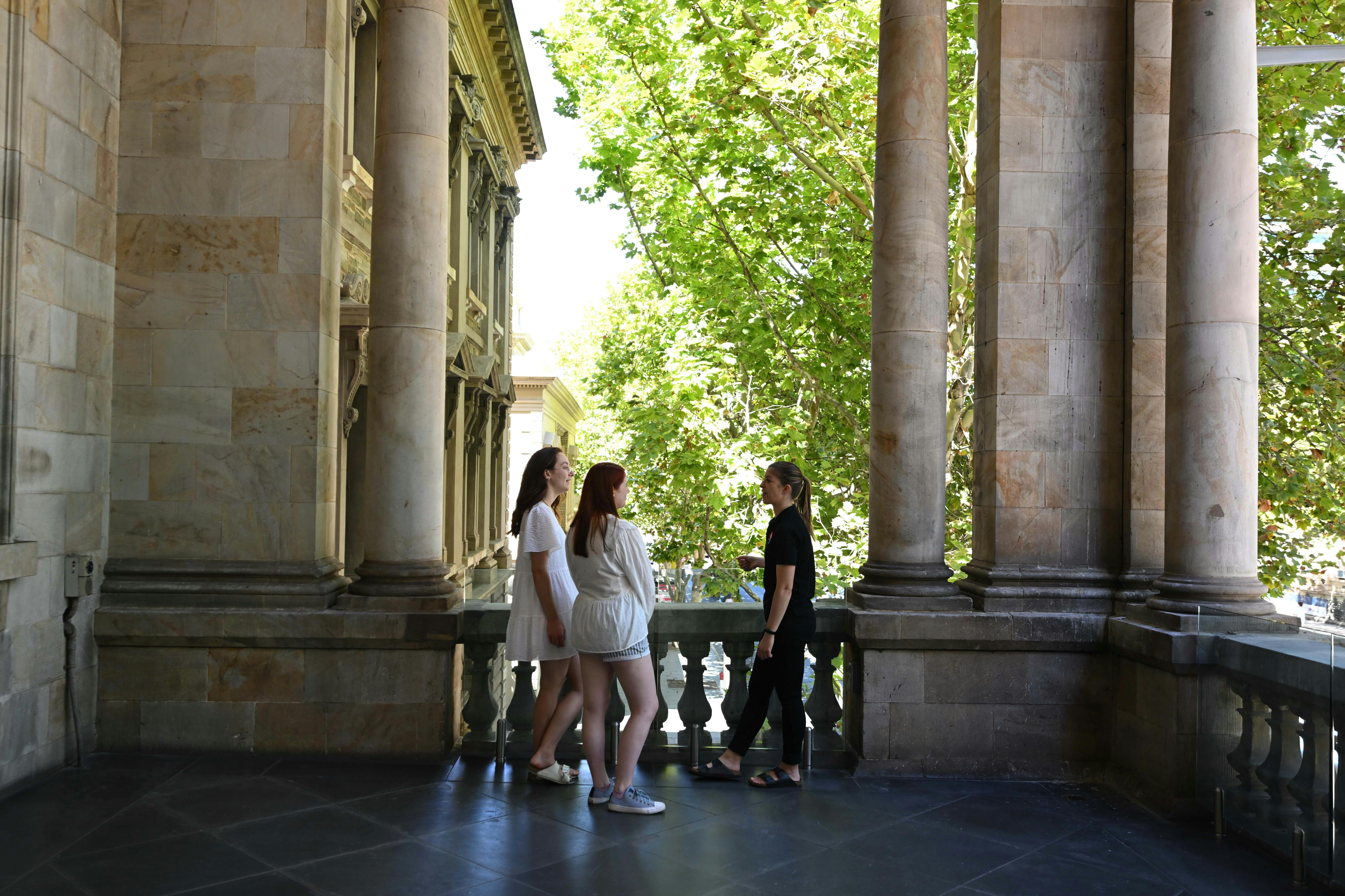 Two travellers and a tour guide chat on a balcony while on the Intimate Walk Adelaide private tour.
