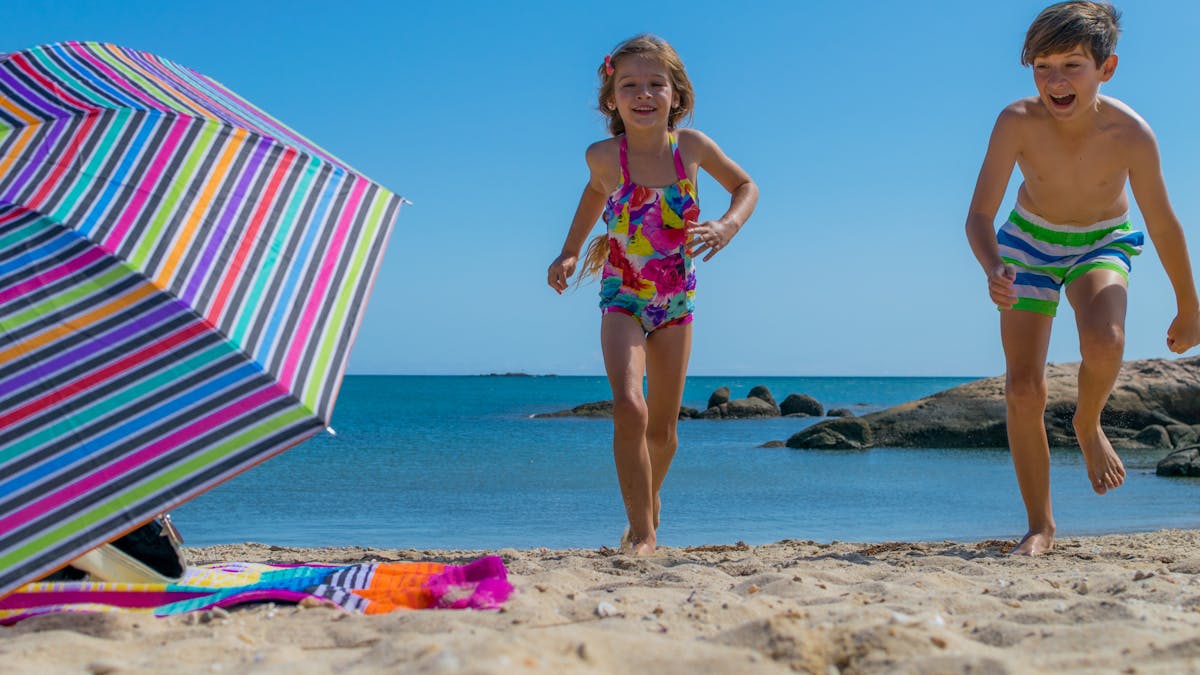 Children playing at sandy beach on sunny day, beach umbrella and beach toys