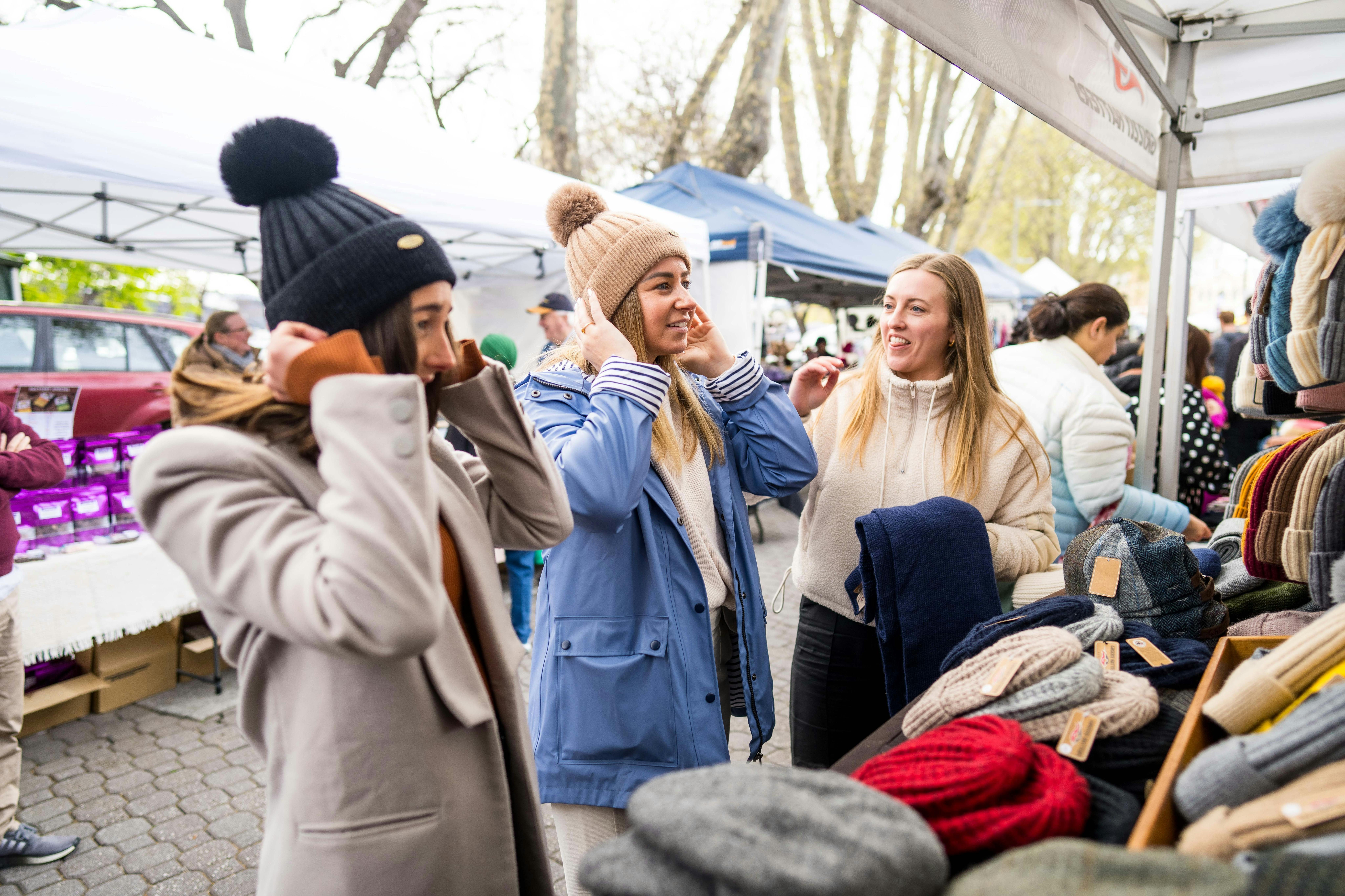 Three girls try on woollen beanies