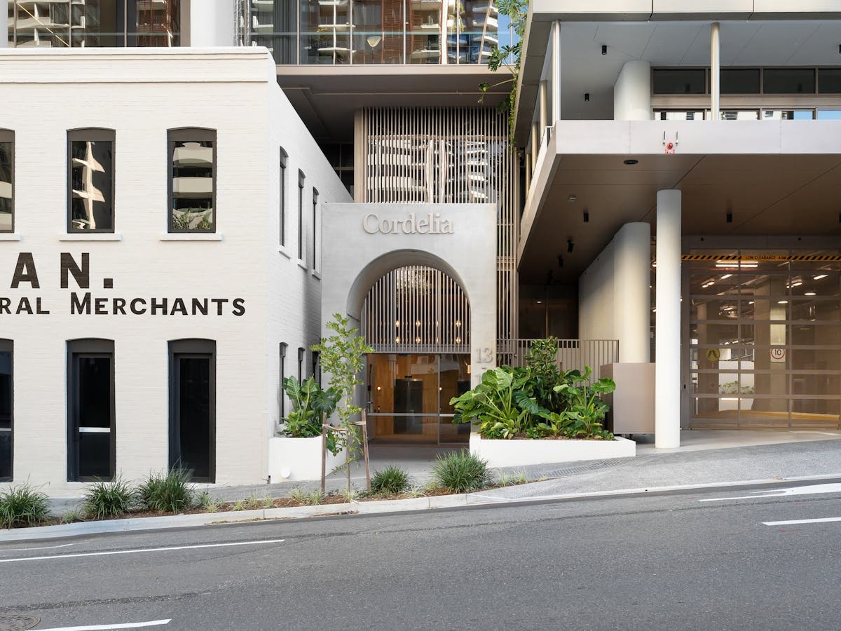 External shot of building with cream coloured facade and archway door. Plants on each side of door.