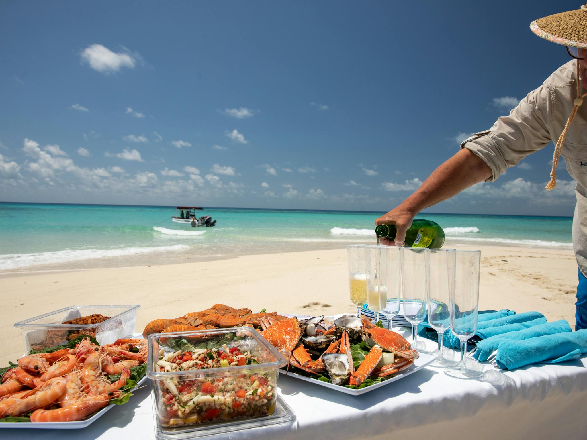 Sparkling apple juice is being poured at a seafood picnic on a tropical beach .