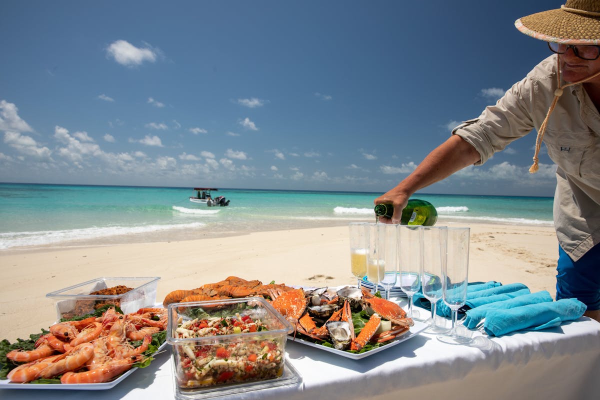 Sparkling apple juice is being poured at a seafood picnic on a tropical beach .
