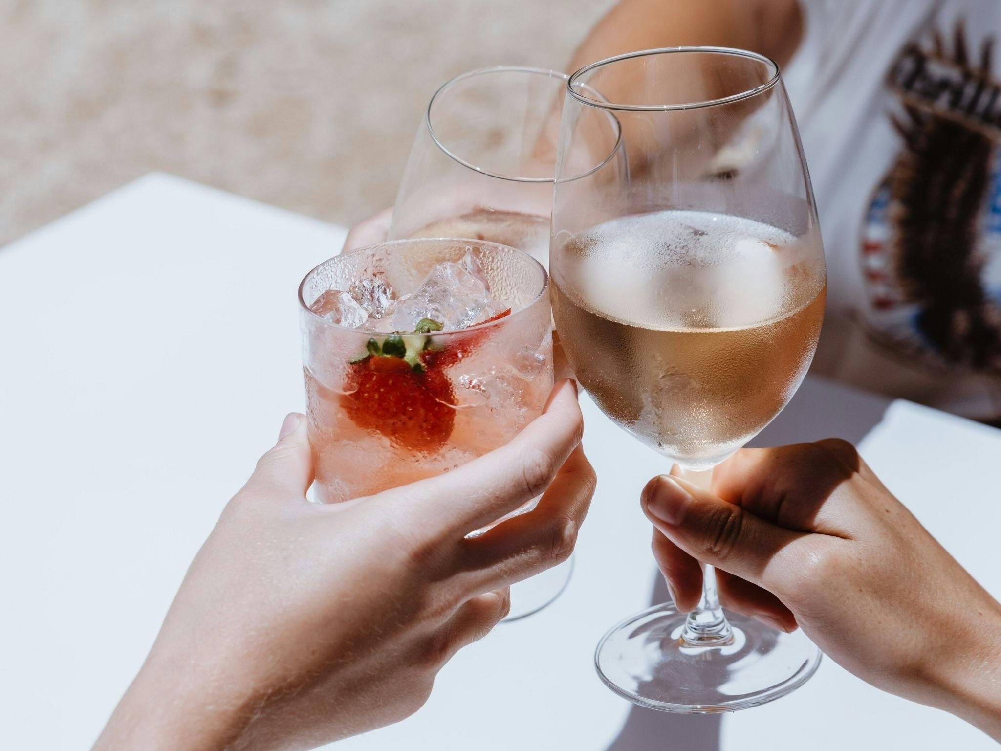 Three hands hold colourful drinks and wine together to 'cheers' at the Cheeky Dog