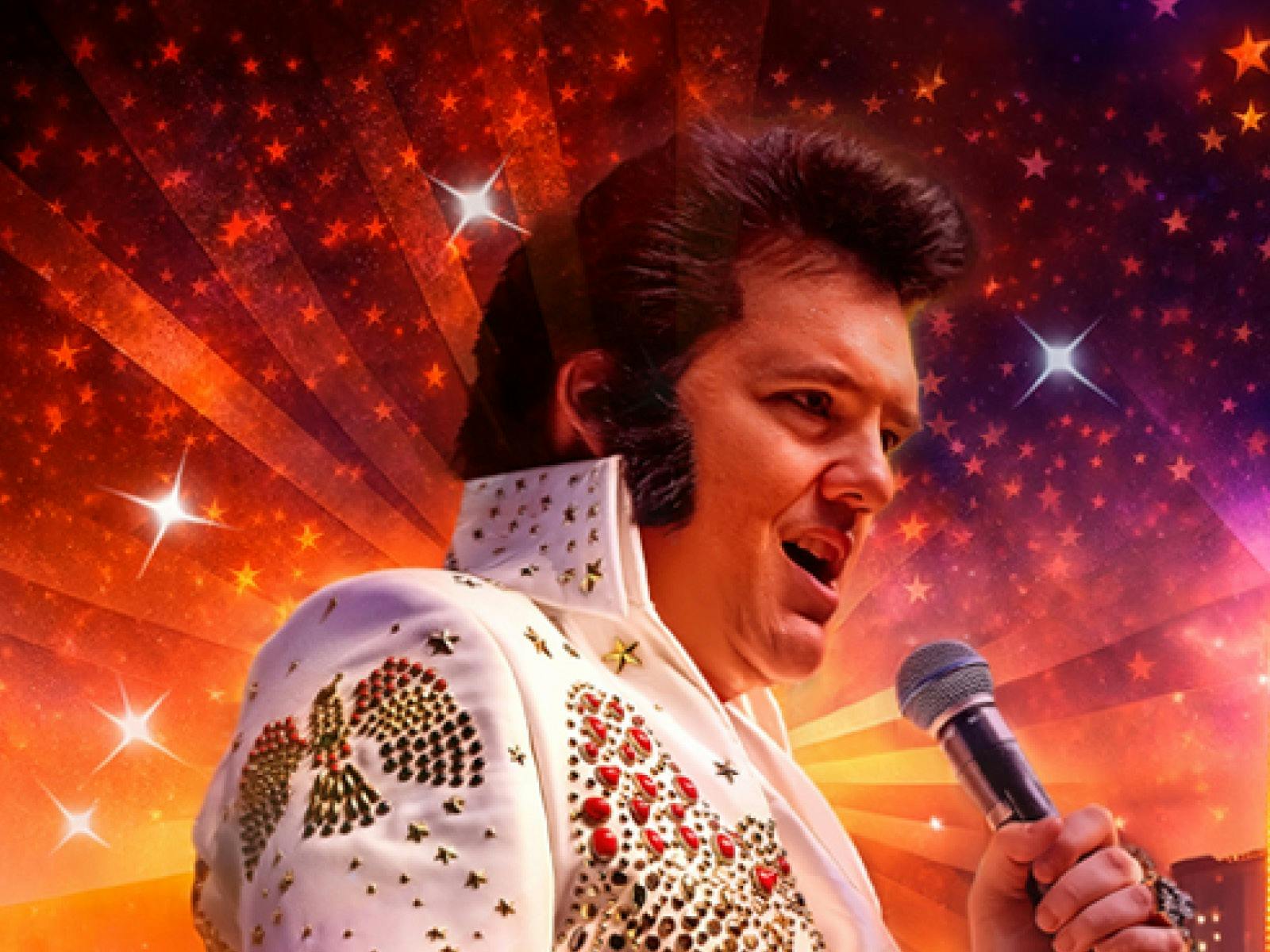 A man dressed in white sparkly jumpsuit with bouffant hair style singing into a microphone