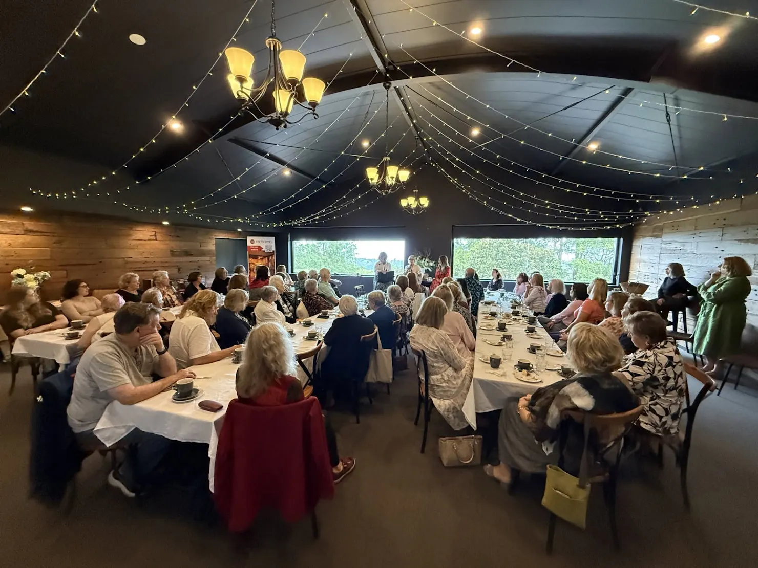 People seated at tables under fairy lights, listening to authors talk