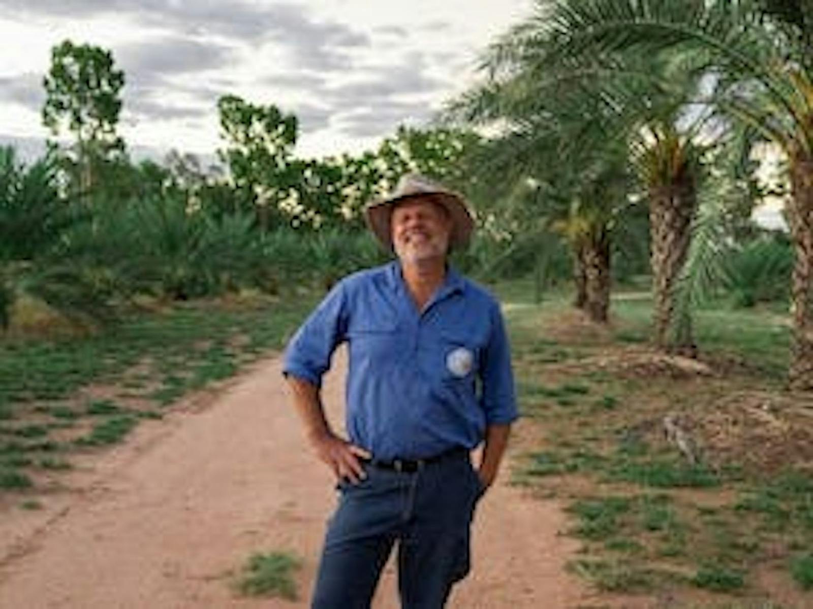 Outback Date Farms owner and tour guide standing between rows of palm trees Outback Date Farms owner and tour guide standing between rows of palm trees