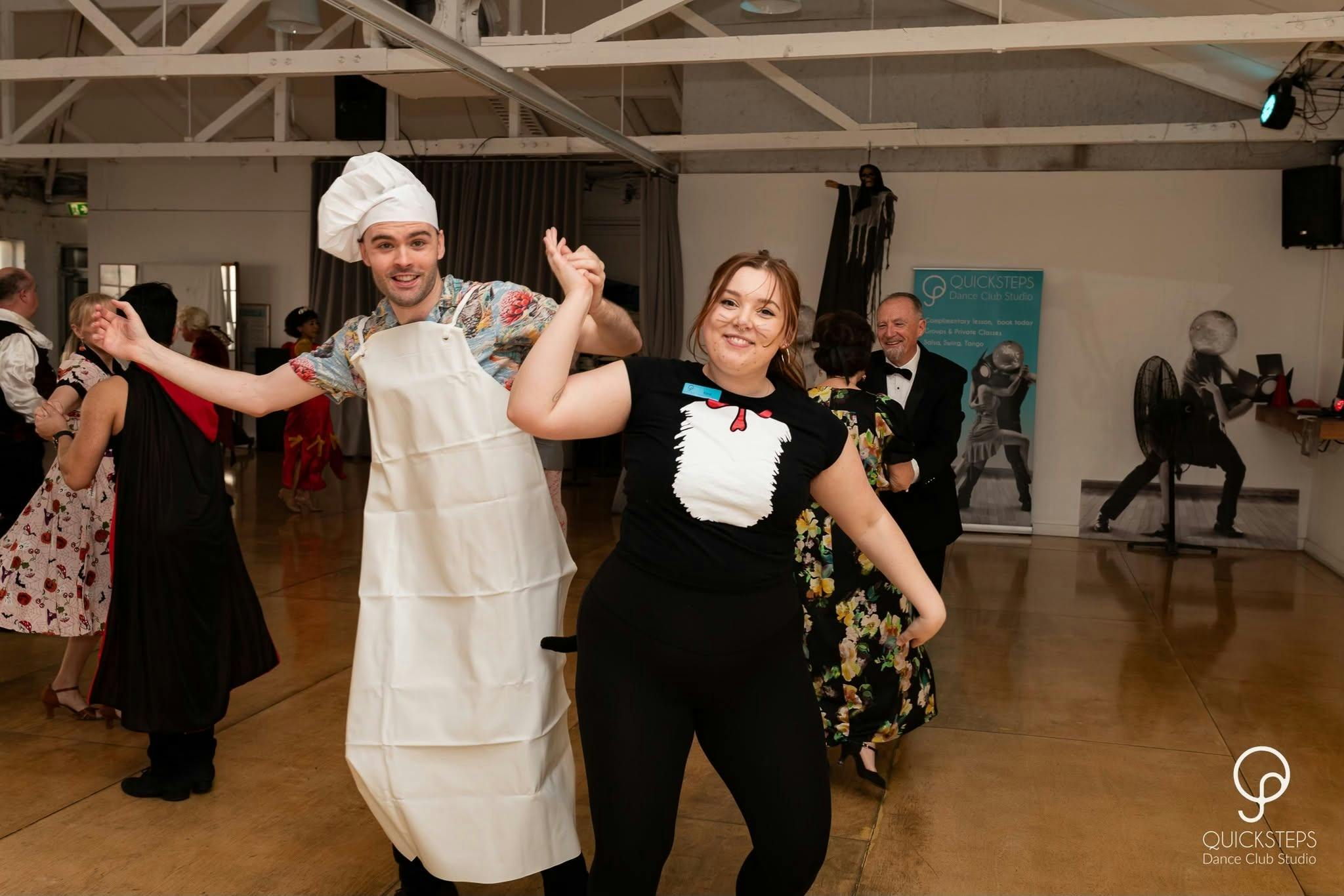 Man and woman dressed up for Halloween Dance Party, holding hands up on the dance floor.