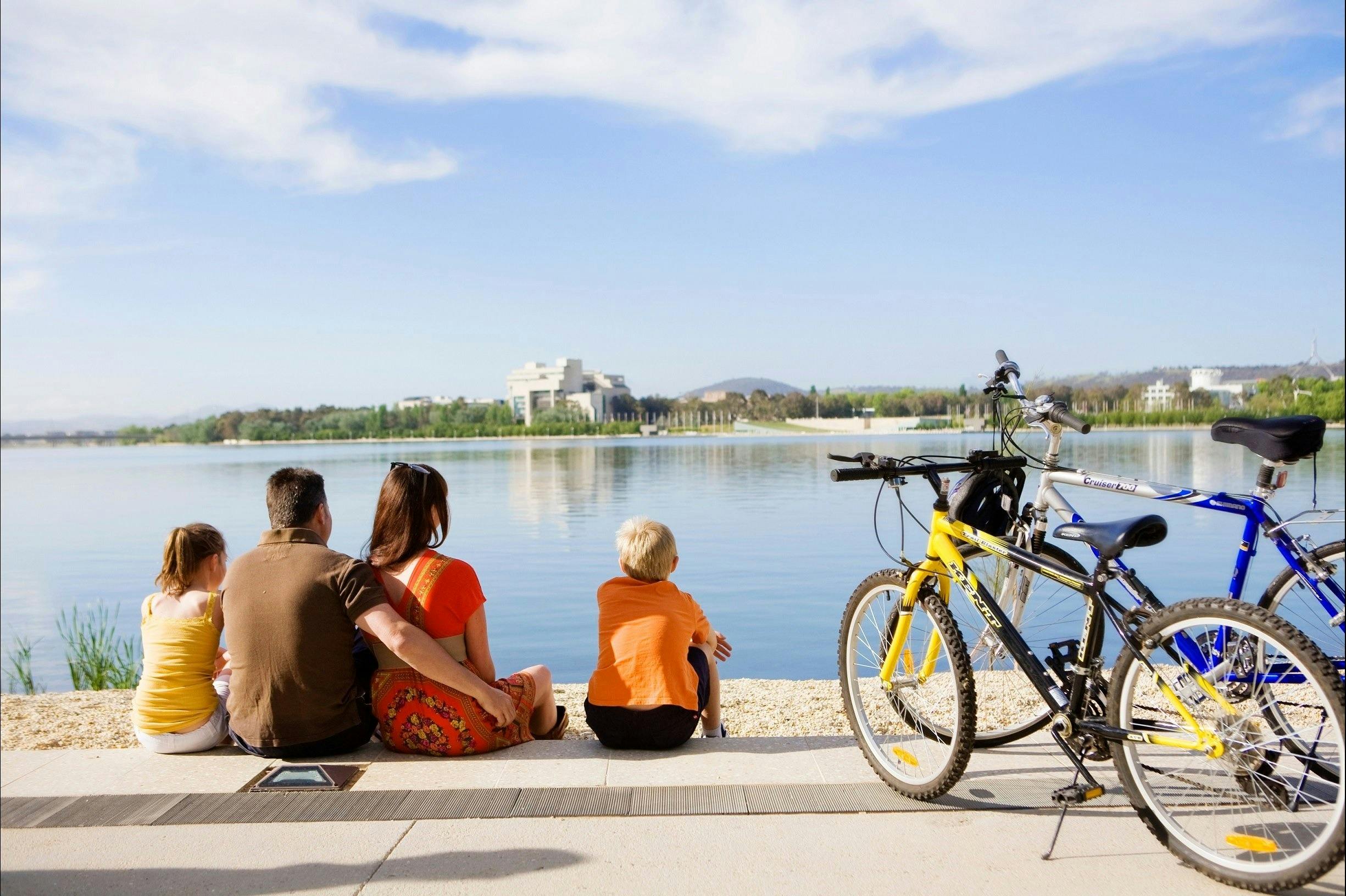 Family sitting on waters edge in Canberra with bikes from Cycle Canberra